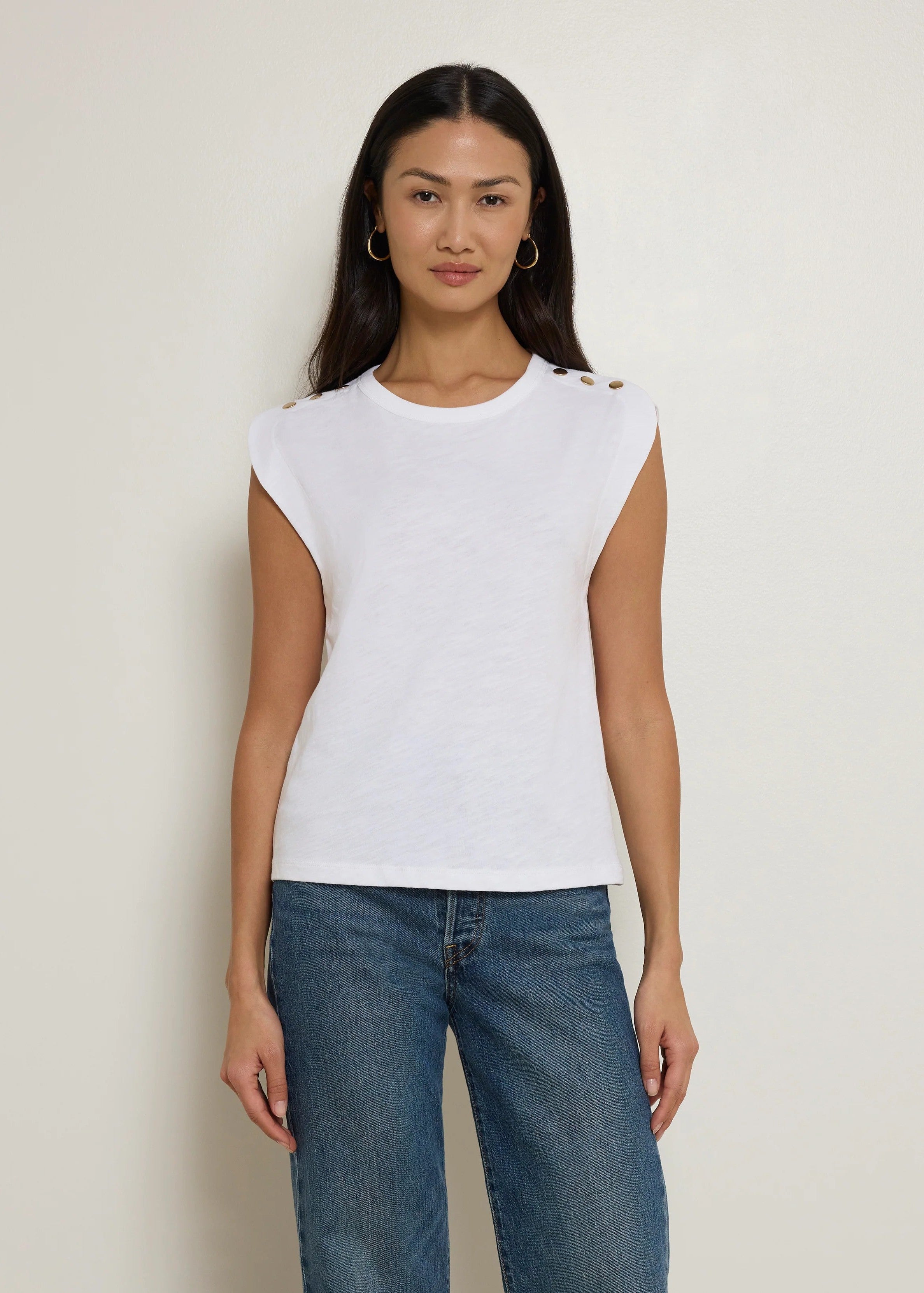 Woman wearing a white sleeveless top and blue jeans against a plain background