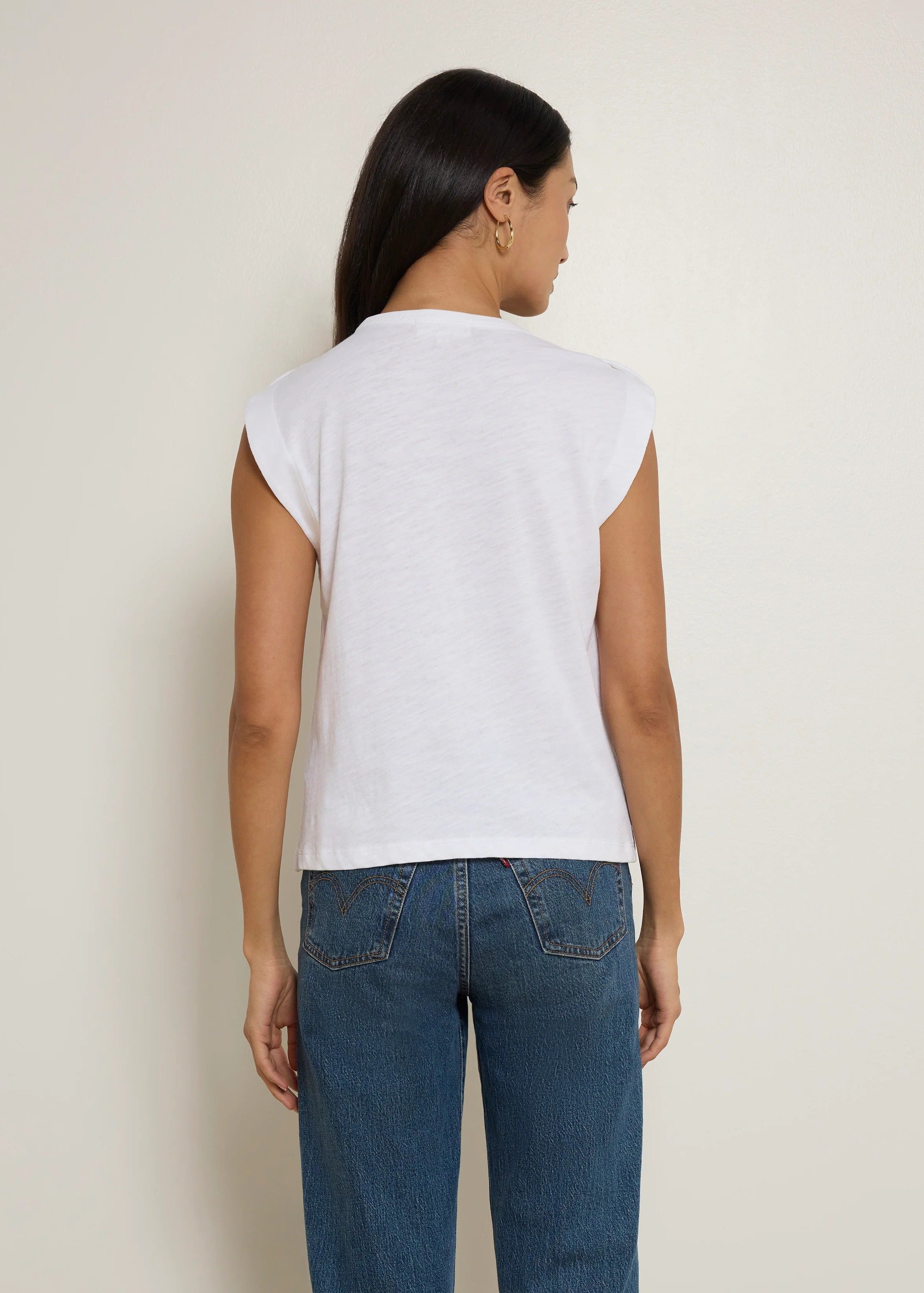 Woman wearing a white sleeveless top and blue jeans against a plain background