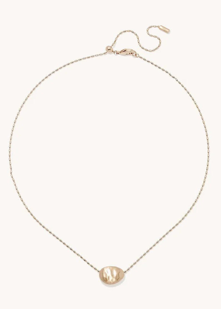 A delicate gold chain necklace with a small, polished gold oval pendant, displayed on a clean off-white background.