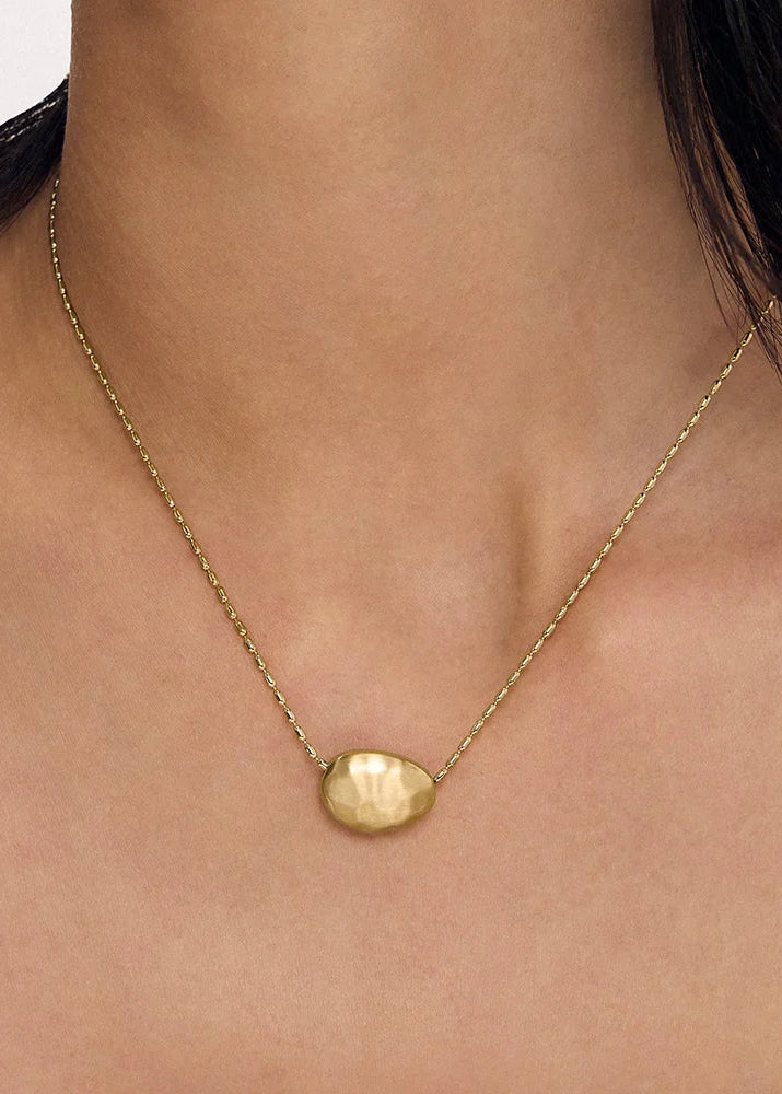 A close-up of a person's neck and upper chest wearing a delicate gold chain necklace with a small, polished gold oval pendant.