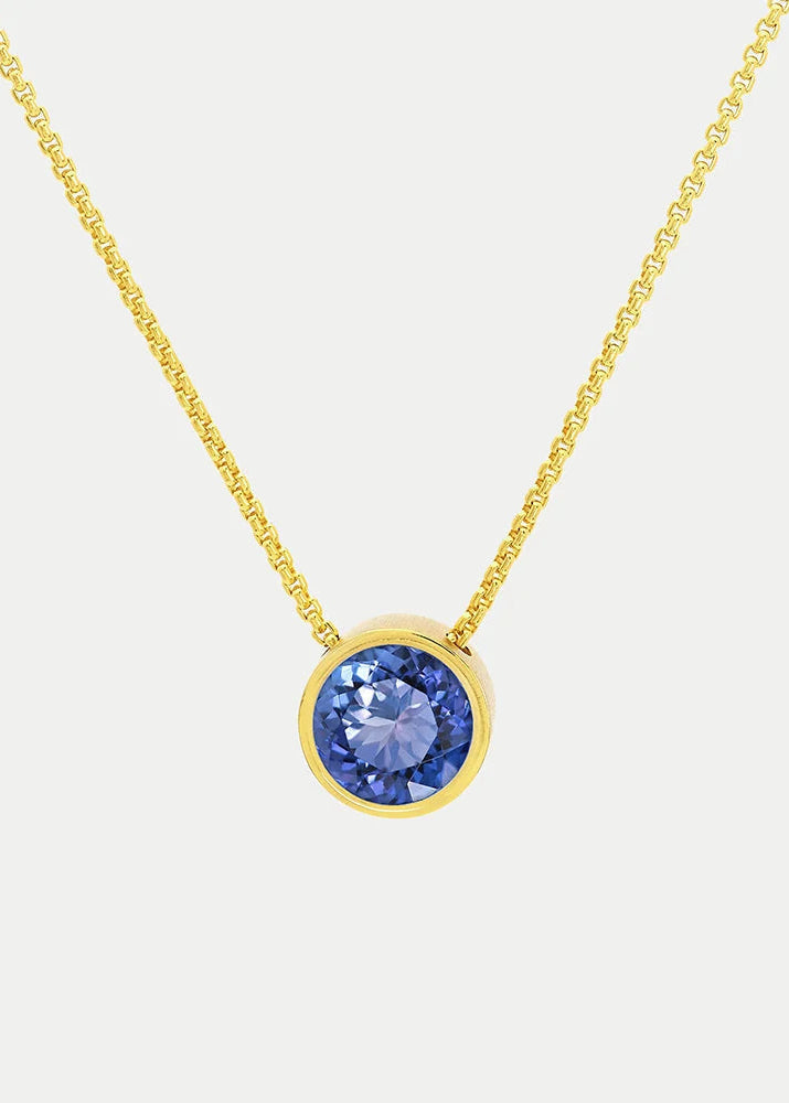 A gold chain necklace with a round bezel-set blue gemstone pendant, shown against a light gray background.