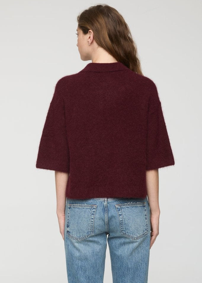 Person wearing a burgundy sweater and blue jeans on a plain background