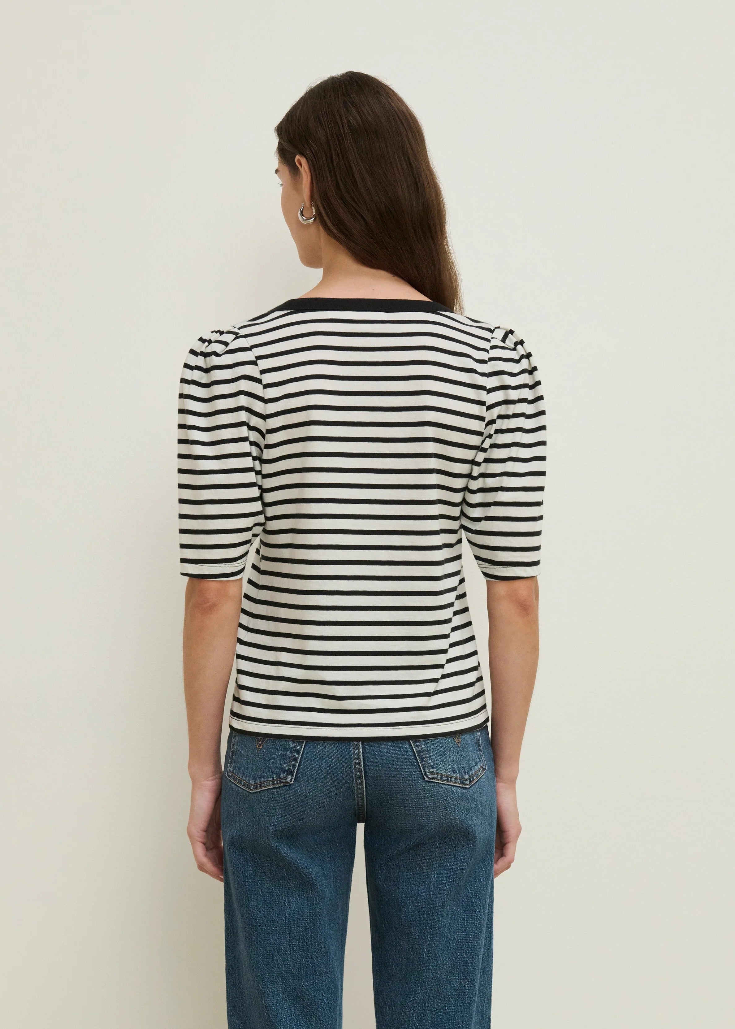 Person wearing a black and white striped shirt and blue jeans against a plain background