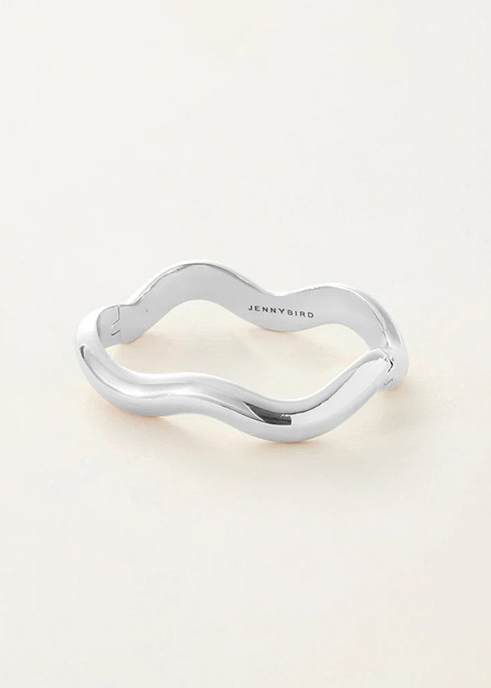 A polished silver wavy bangle bracelet with the brand name 'JENNYBIRD' engraved on the inside, displayed on a clean, light beige background.