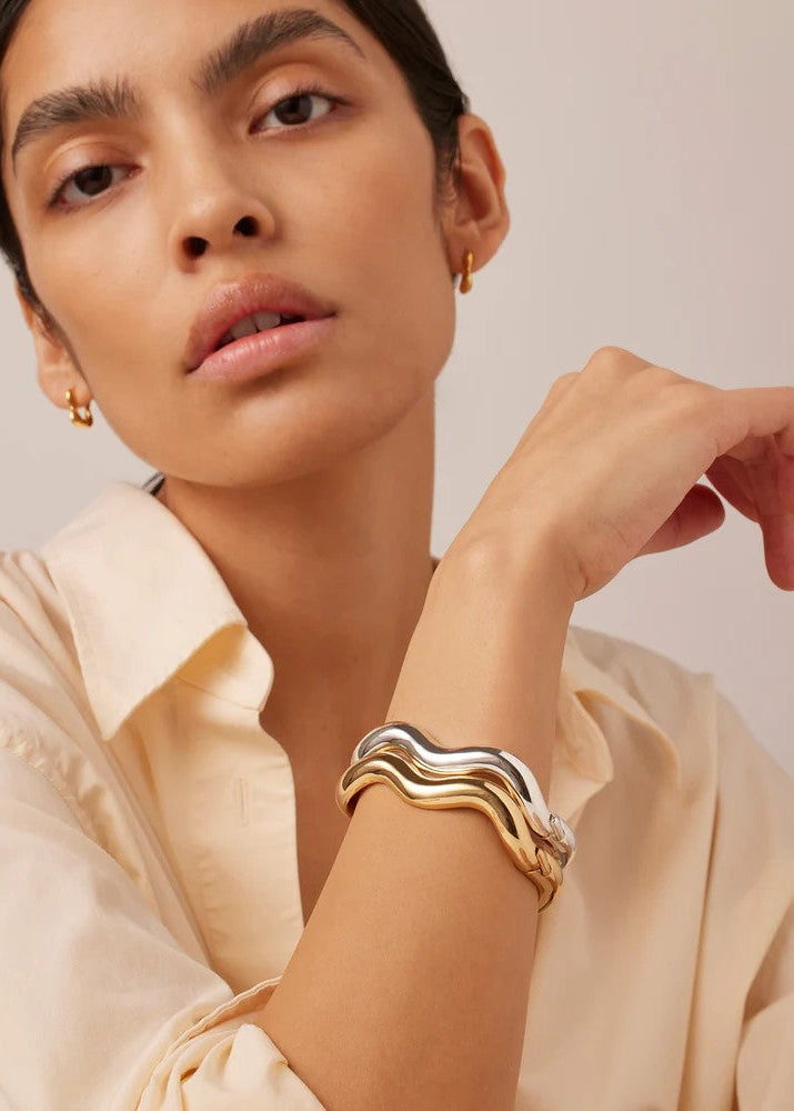 Woman wearing a gold bracelet and earrings against a neutral background