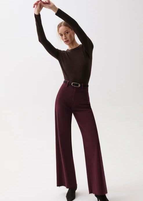 A model posing in a dark brown long-sleeve top and deep burgundy wide-leg trousers with a black belt, set against a plain white studio background.