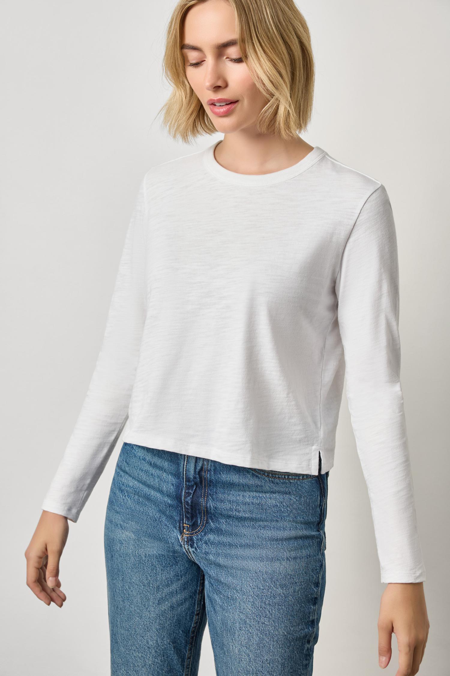 Woman wearing a white long-sleeve top and blue jeans on a plain background