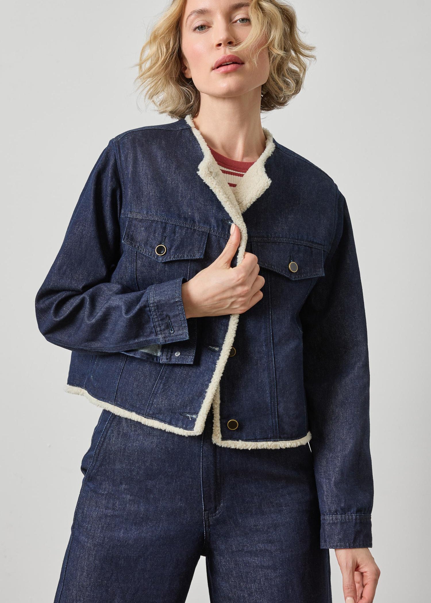 Woman wearing a blue denim jacket with white trim on a light gray background