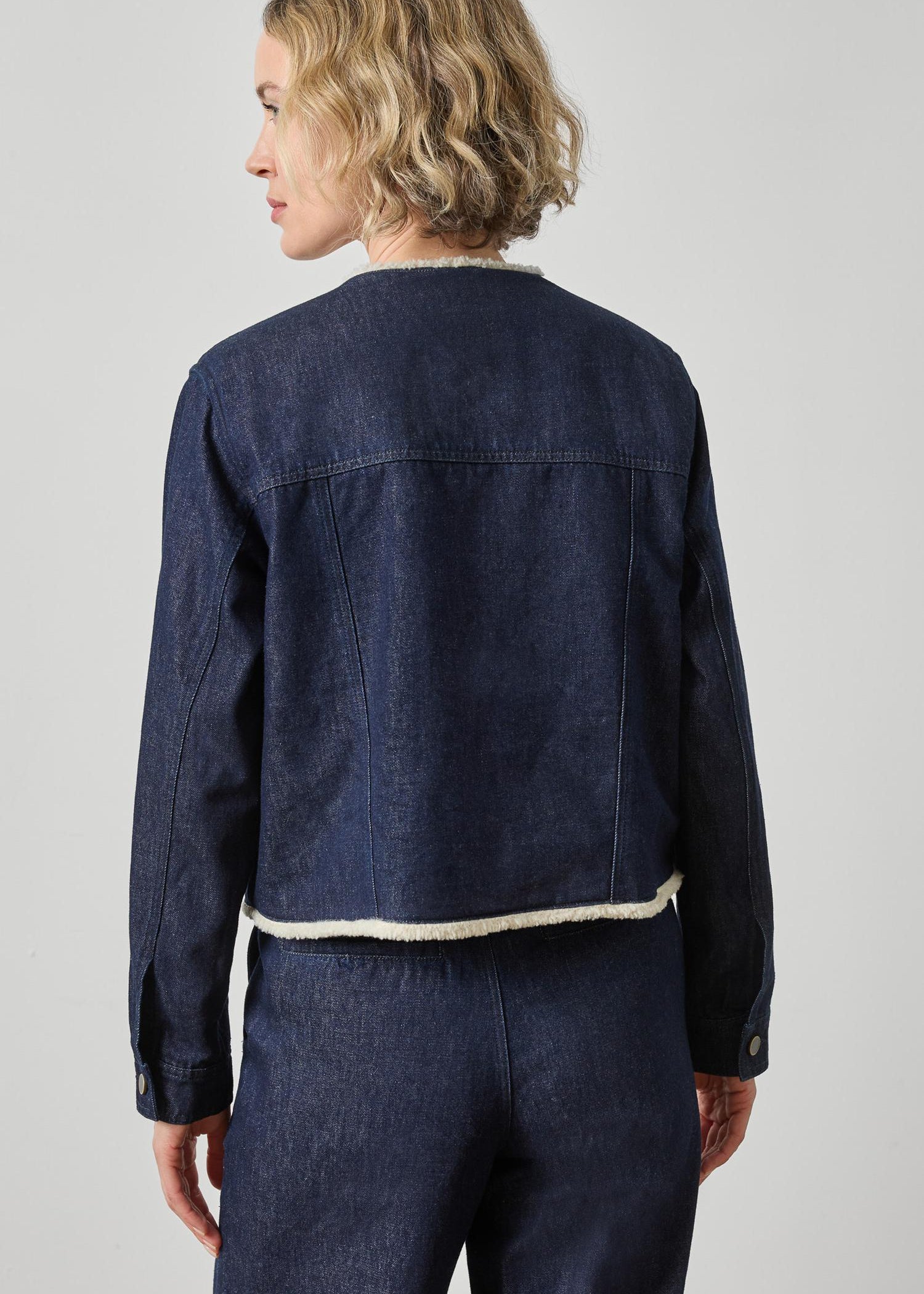 Person wearing a dark denim jacket and pants on a light gray background