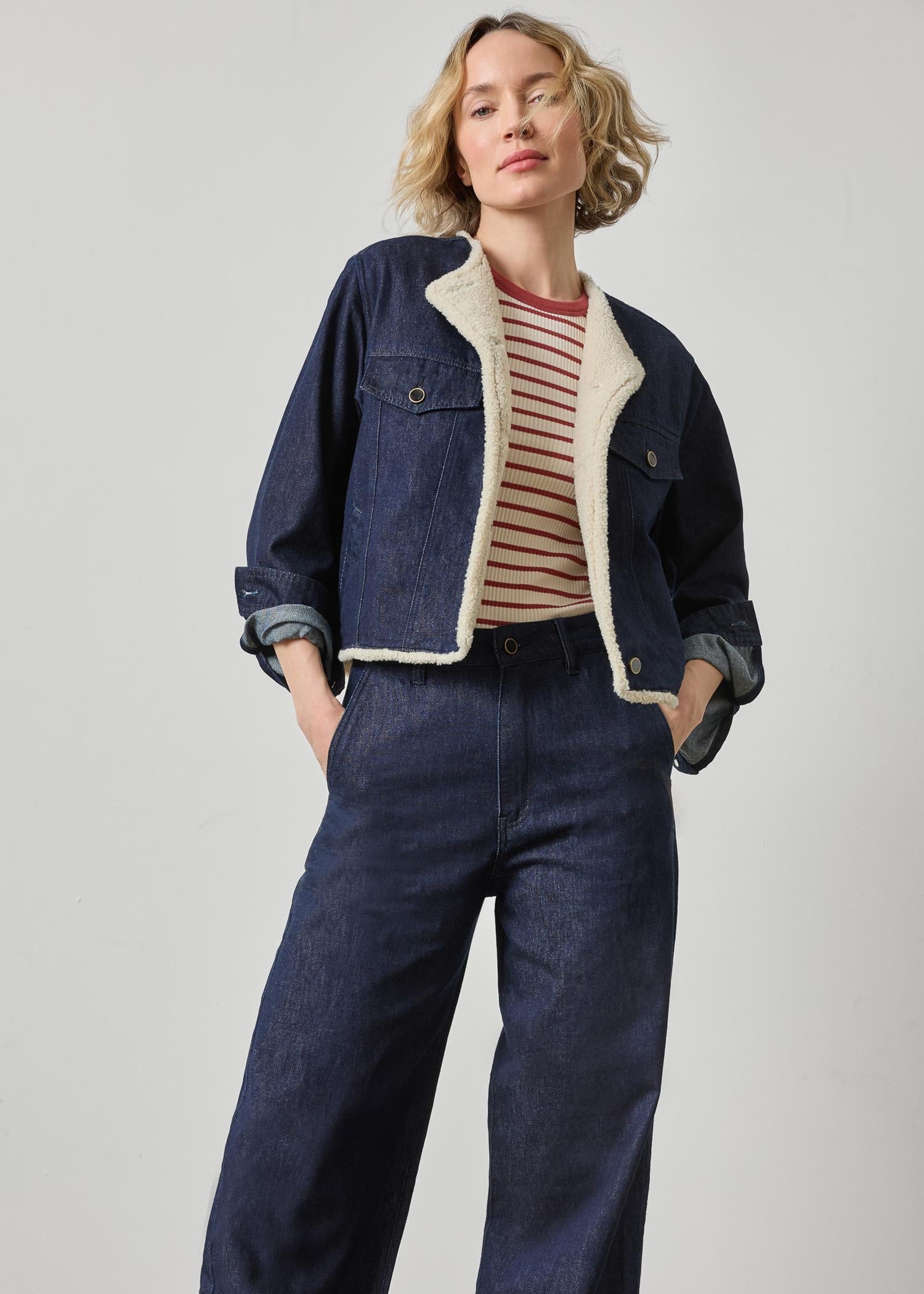 Woman wearing a denim jacket and pants with a striped shirt on a plain background