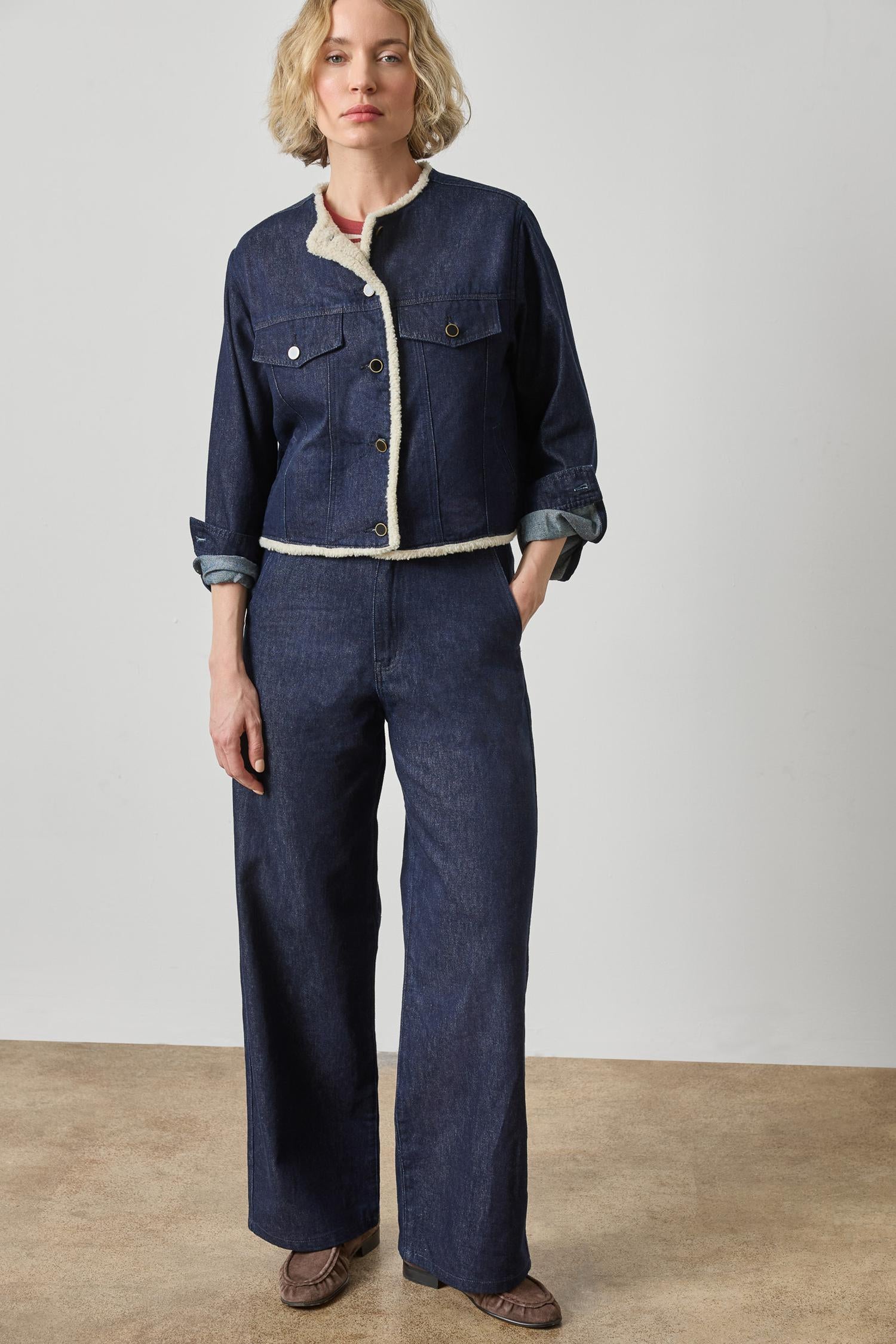 Woman wearing a denim outfit with a white shirt underneath on a plain background