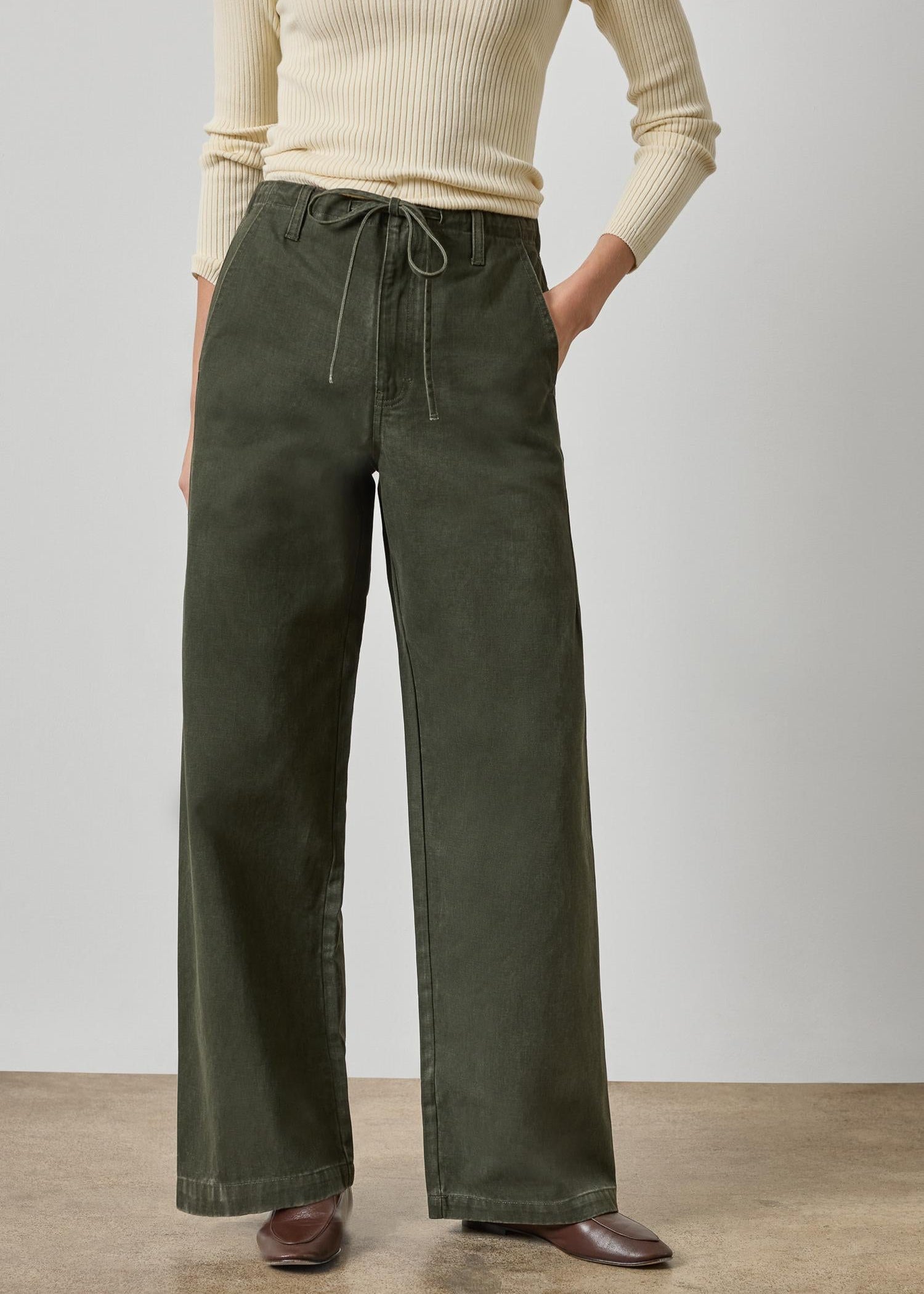 Person wearing olive green wide-leg pants with a beige top on a plain background