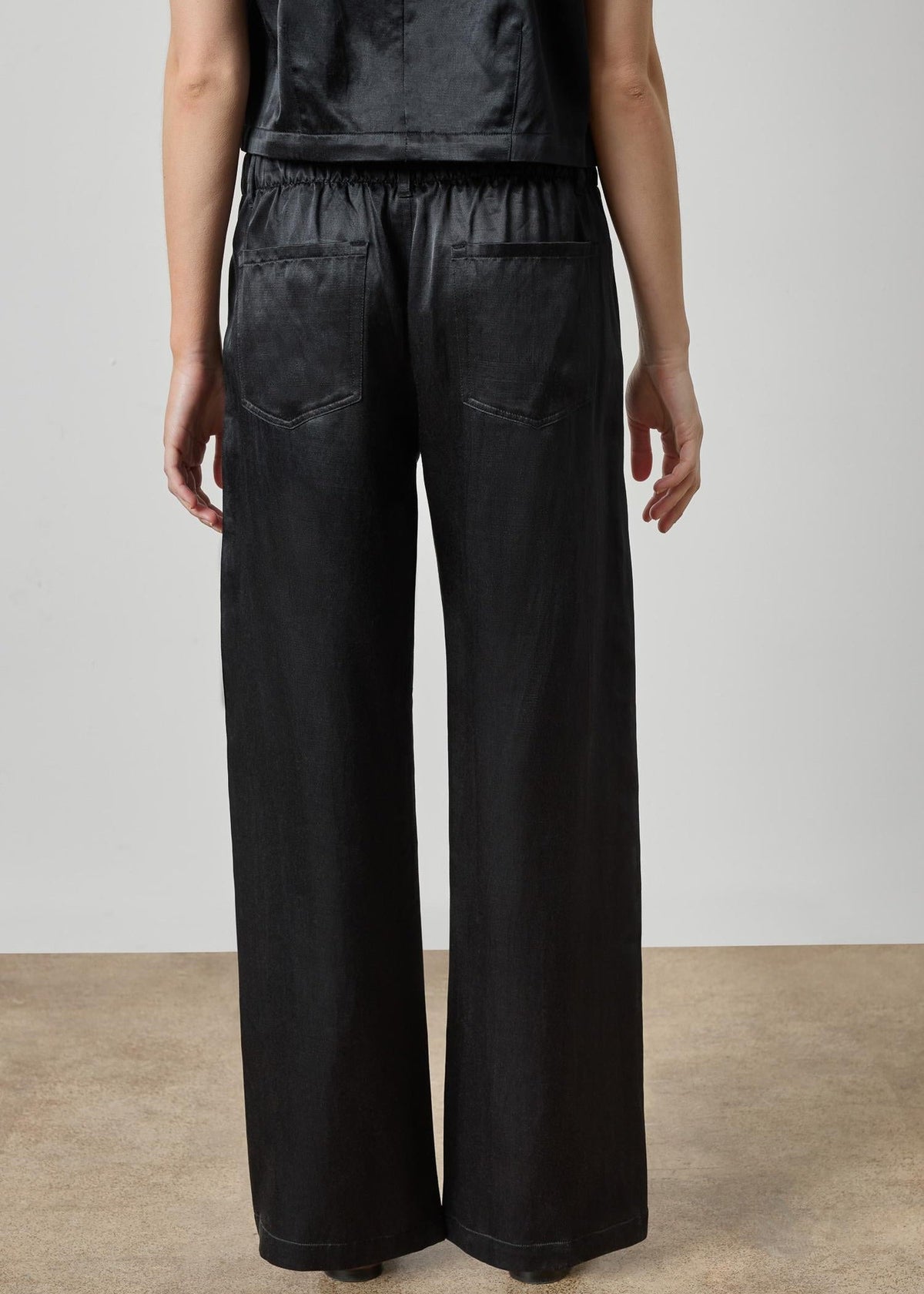 Person wearing black wide-leg pants and a black top against a plain background