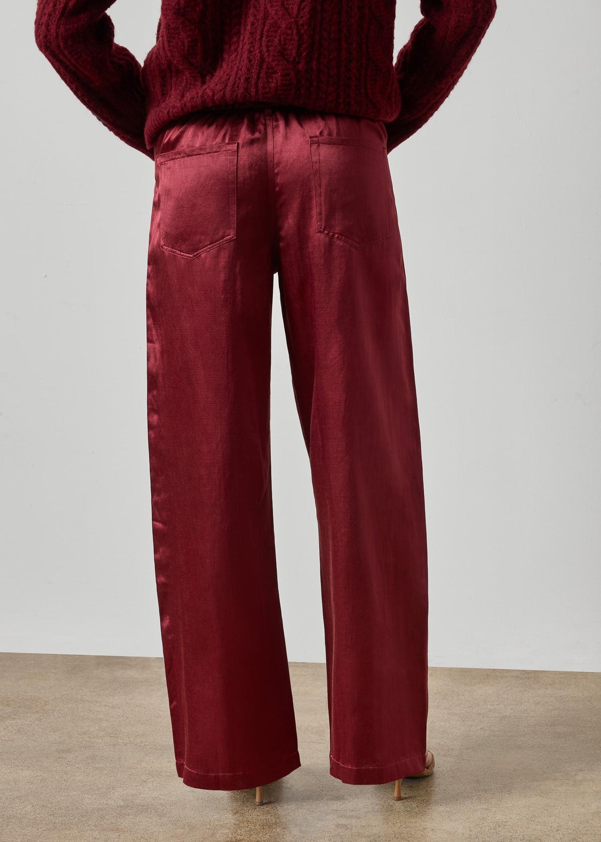 Person wearing a burgundy sweater and wide-leg pants against a plain background