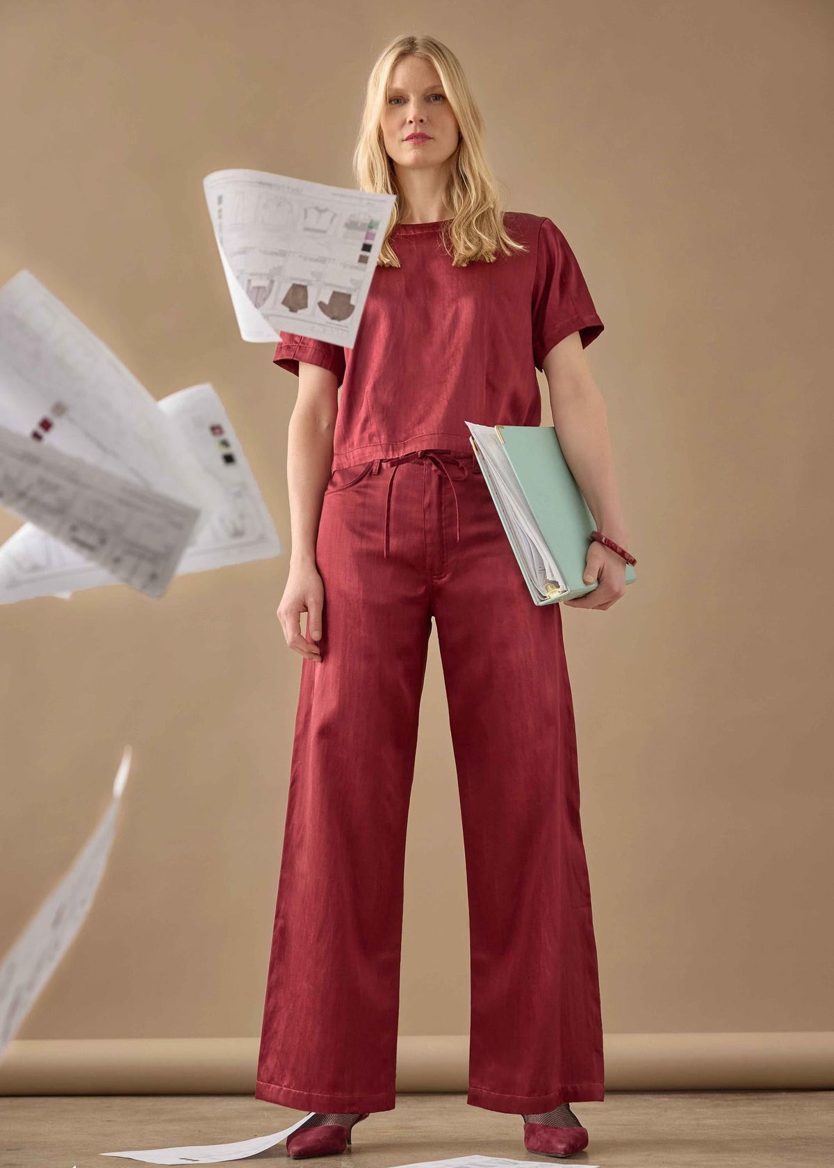 Woman in red outfit holding papers against a beige background