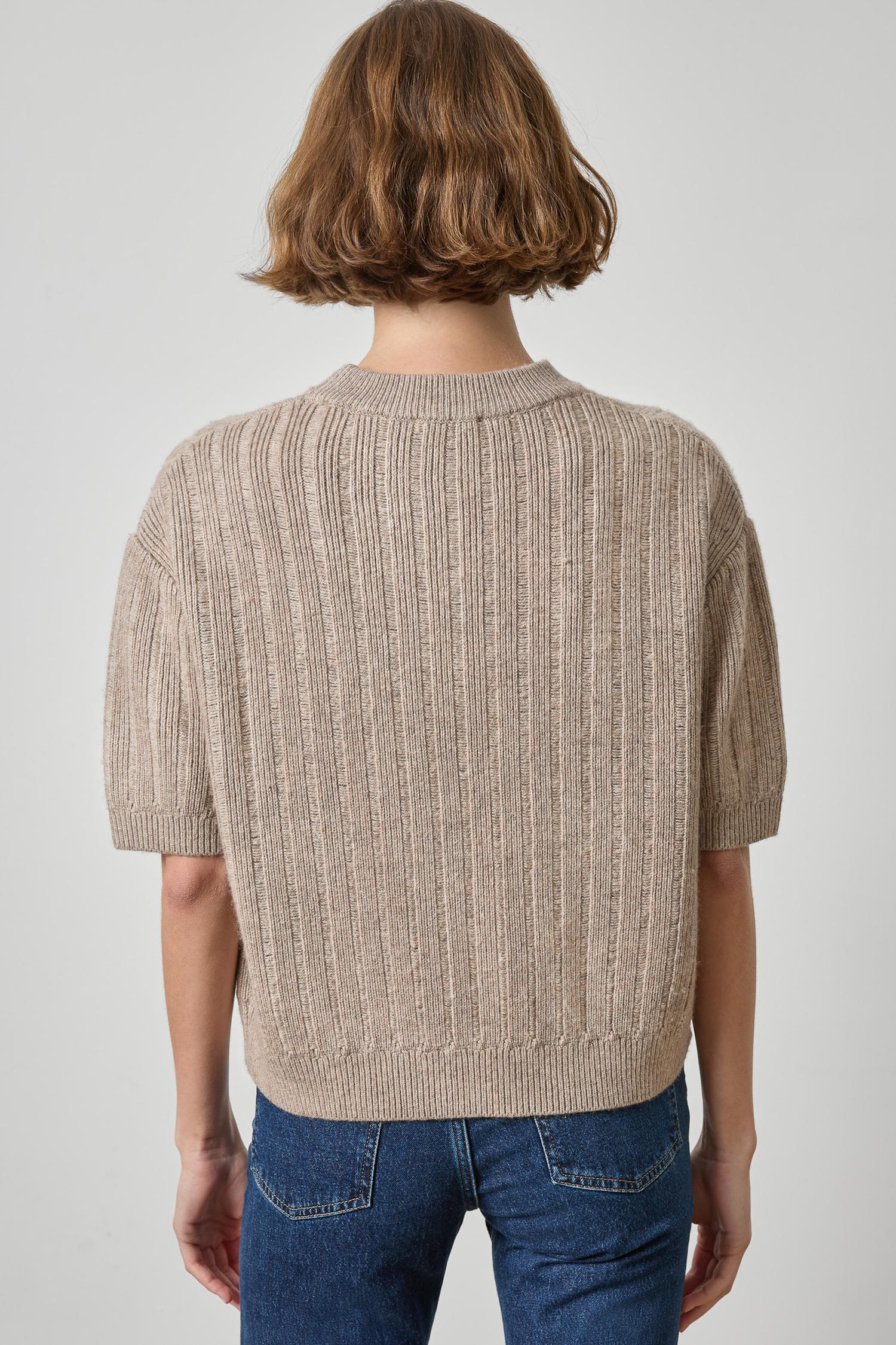 Person wearing a beige knitted sweater and blue jeans on a plain background