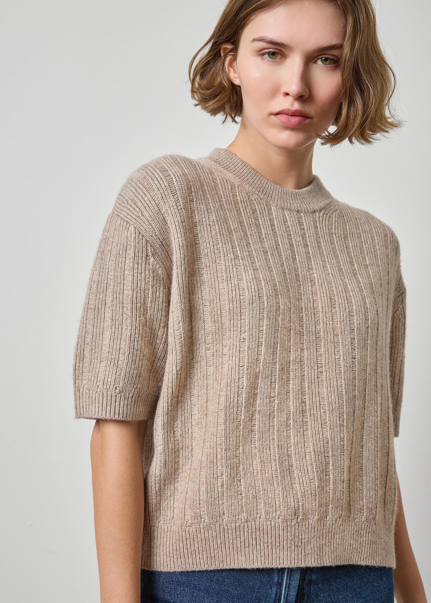 Woman wearing a beige ribbed sweater against a plain background