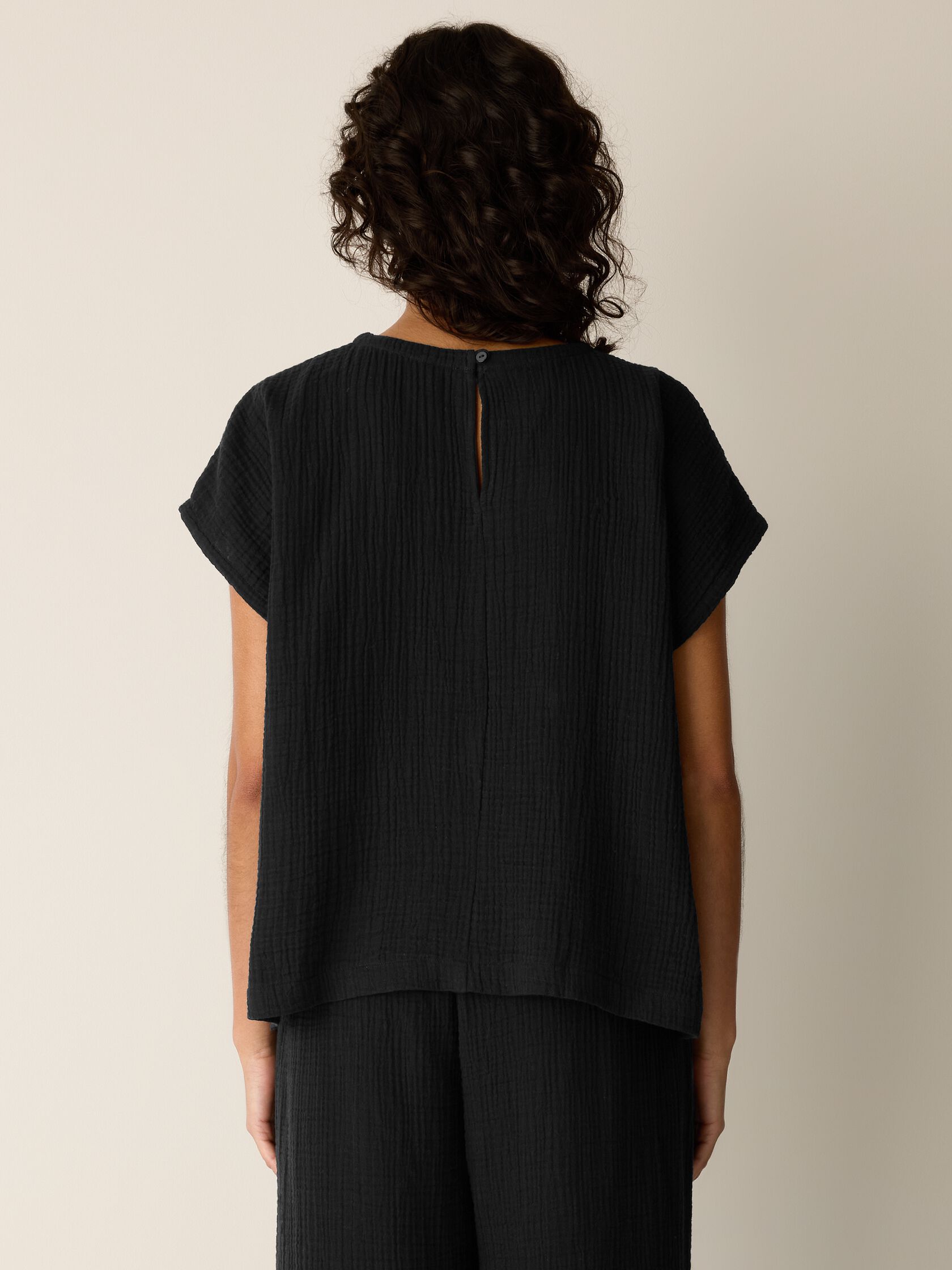 Person wearing a black top and pants against a neutral background