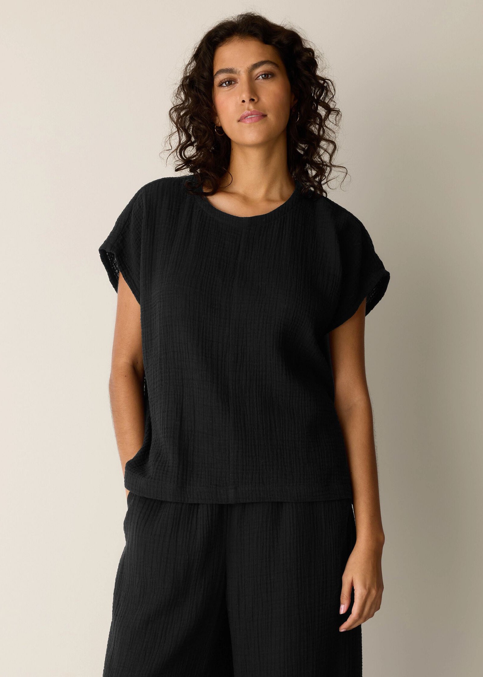Woman wearing a black top and black pants against a neutral background