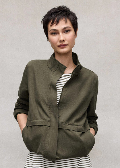 Woman wearing an olive green jacket over a striped shirt against a plain background