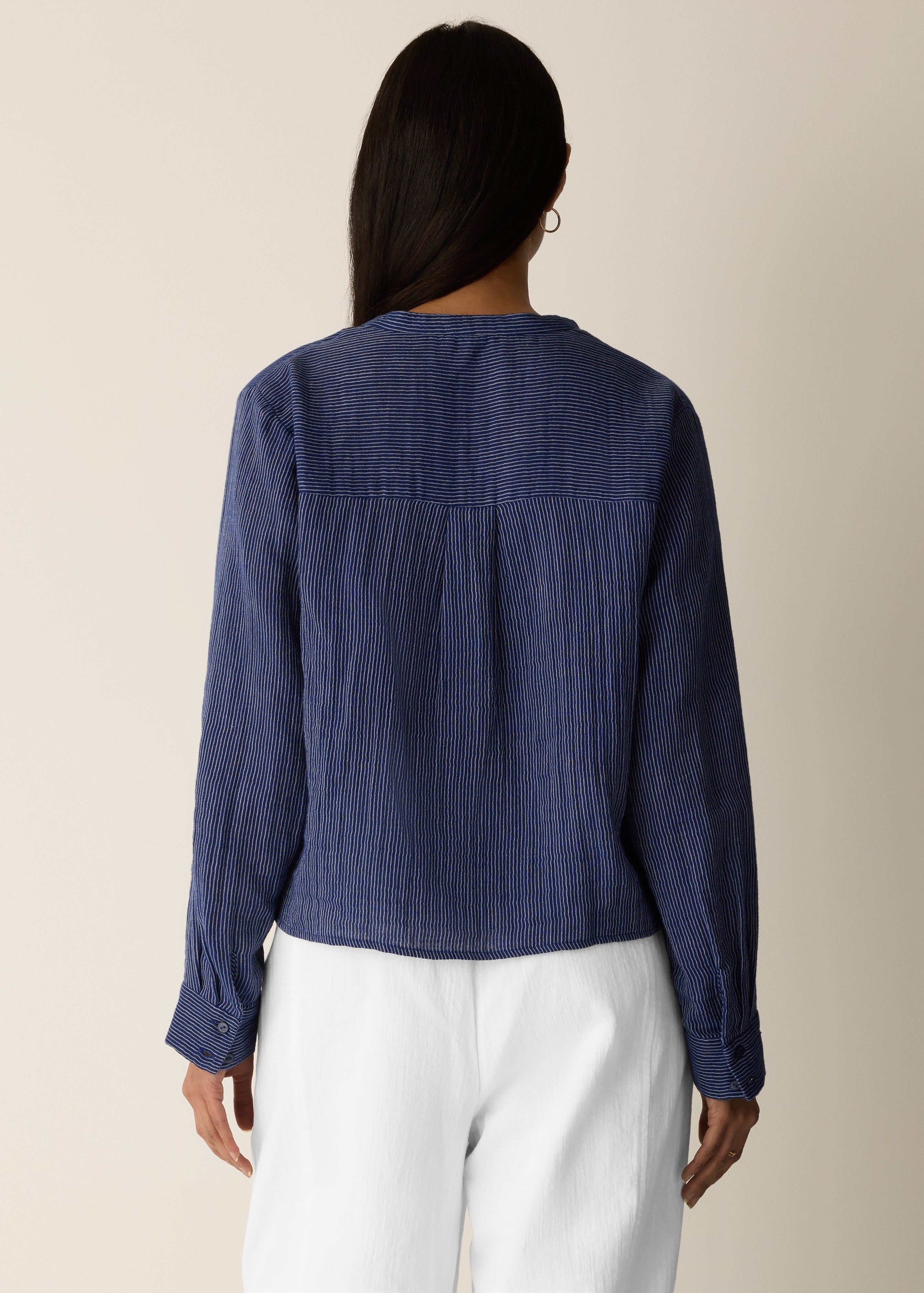 Person wearing a blue textured blouse and white pants on a beige background