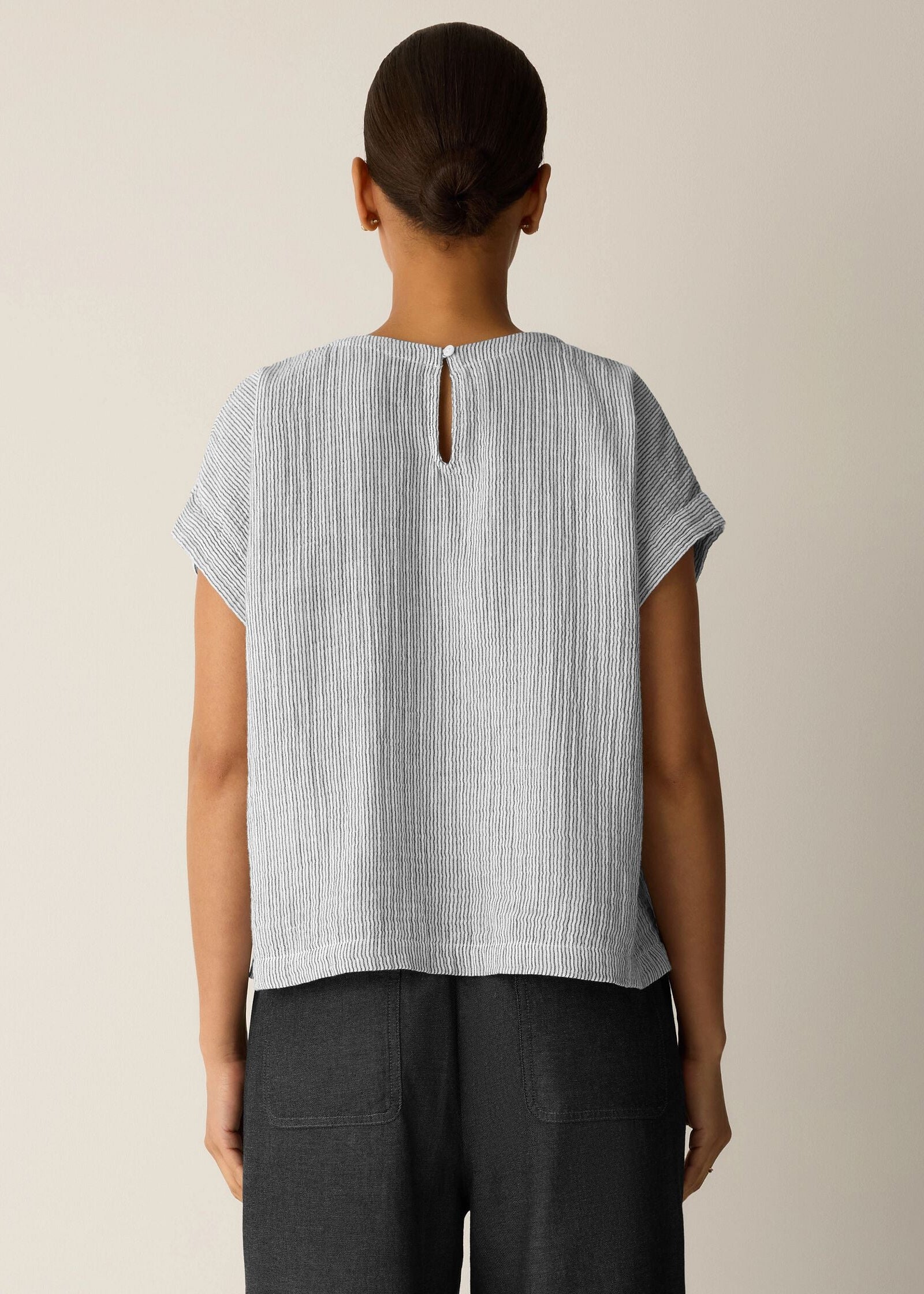 Person wearing a light gray textured top with a cut-out back design on a beige background