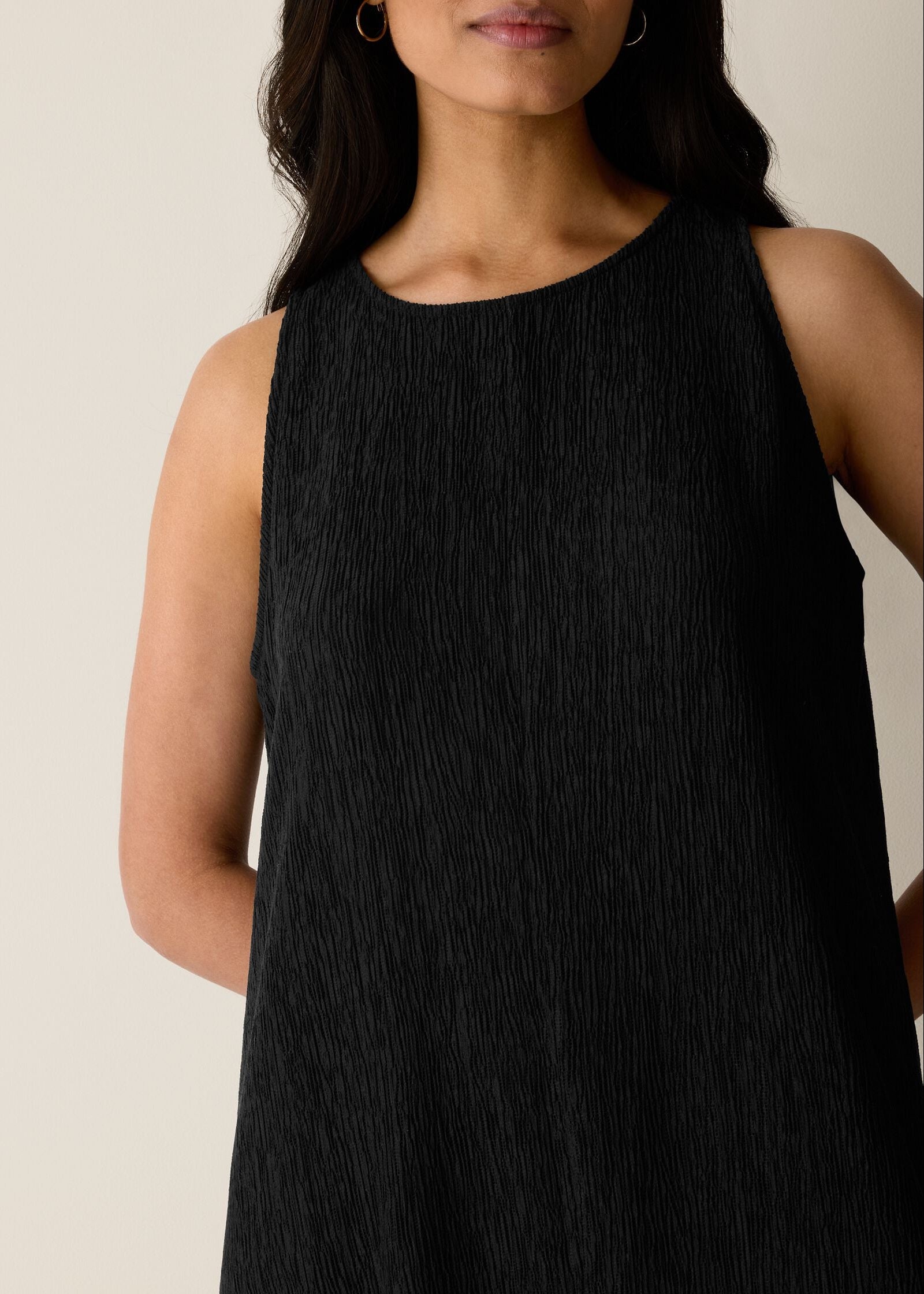 Woman wearing a black sleeveless dress against a neutral background