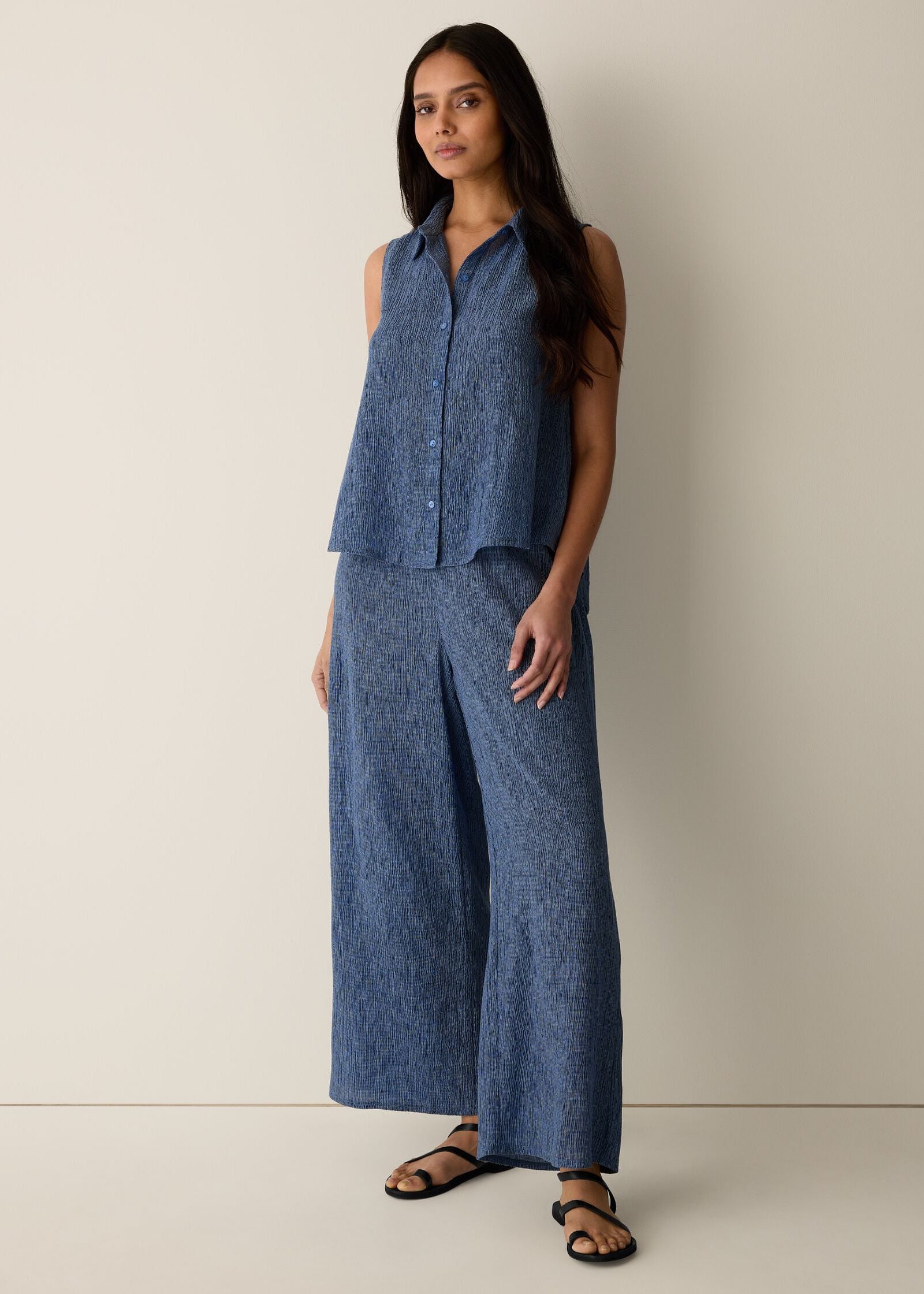 Woman wearing a blue sleeveless top and wide-leg pants against a plain background
