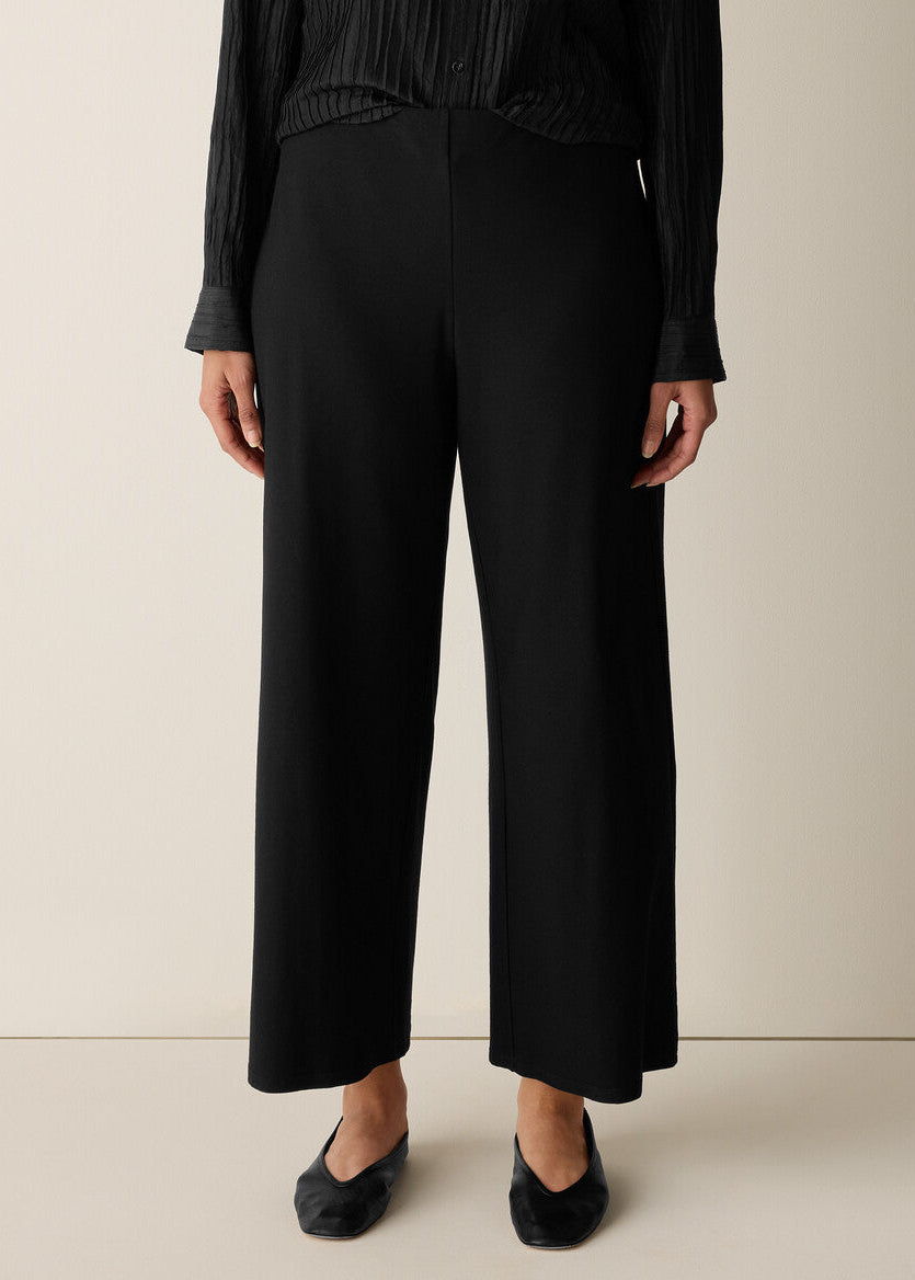 Person wearing black wide-leg pants and a black top on a beige background