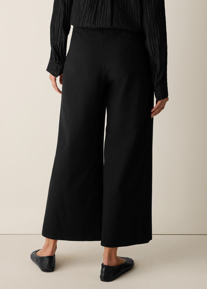 Person wearing black wide-leg pants and a black top on a beige background