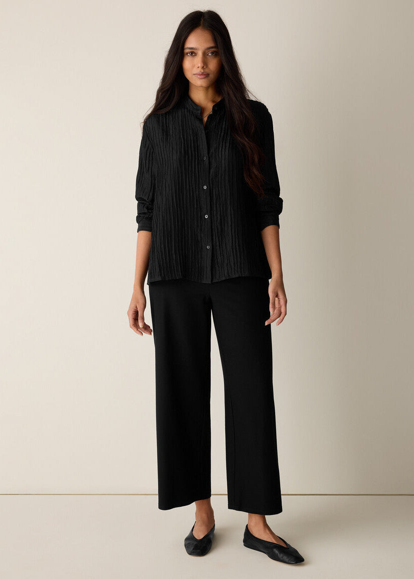 Woman wearing a black button-up shirt and wide-leg pants against a neutral background