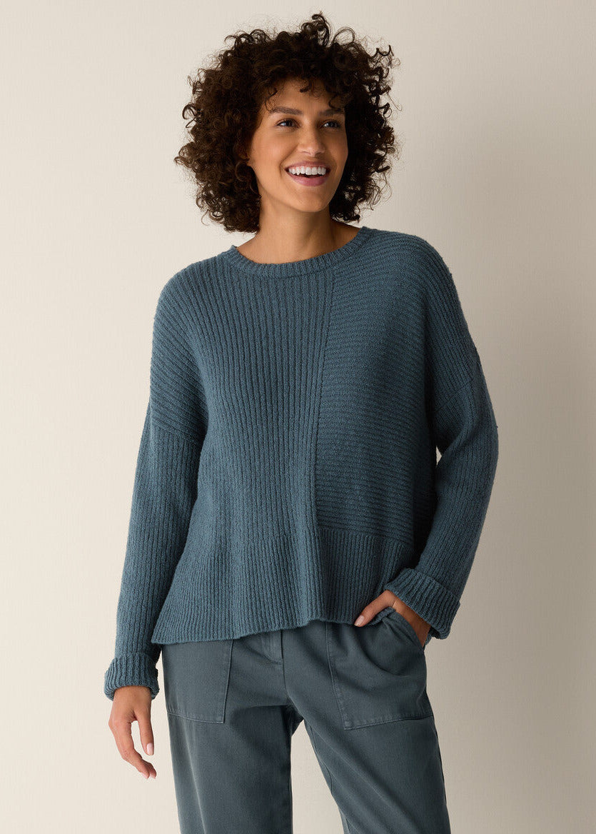 Woman wearing a teal sweater and pants against a beige background