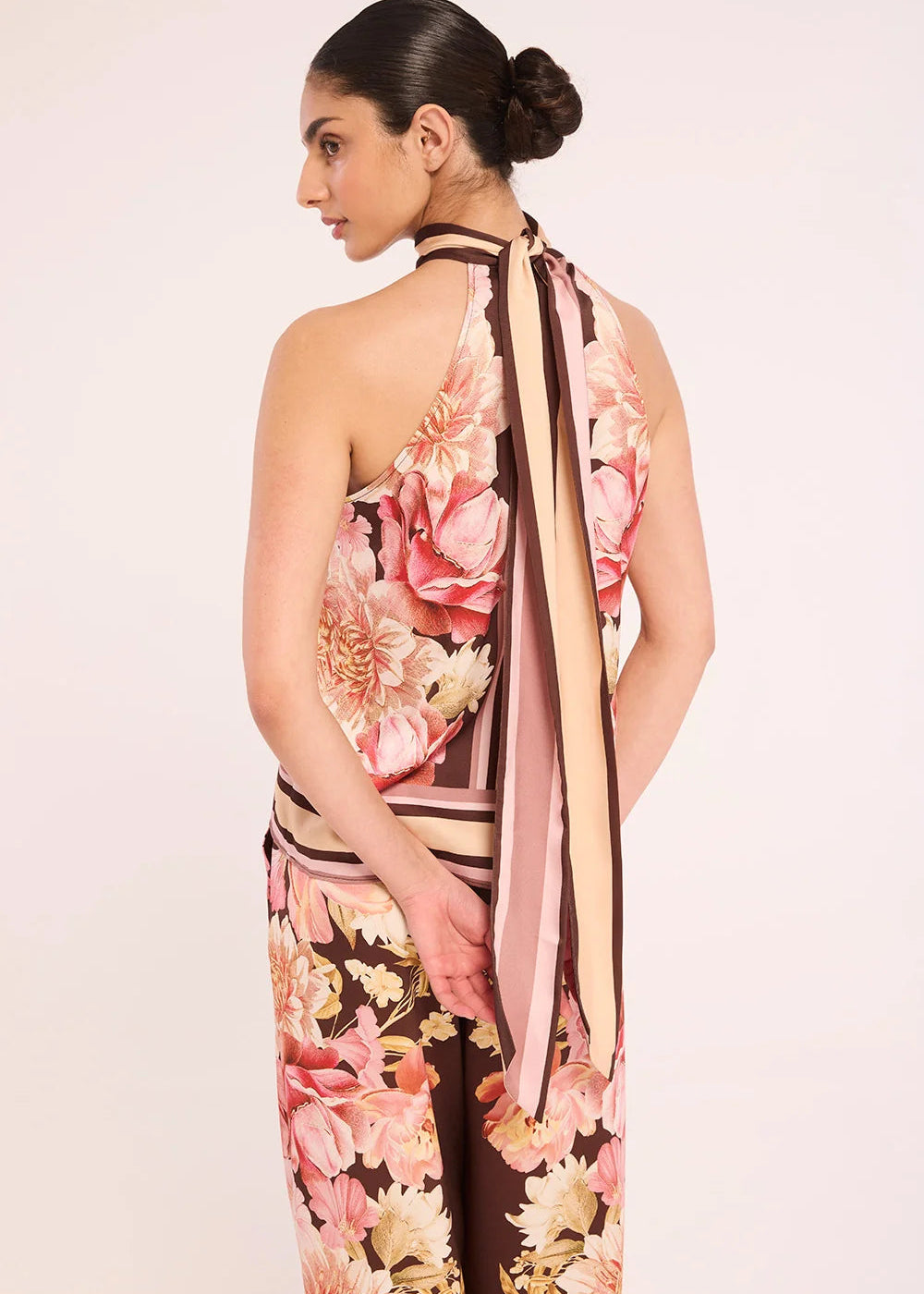 A woman shown from the back wearing a halter-neck dress with a pink, beige, and brown floral print and striped details, set against a plain light background.