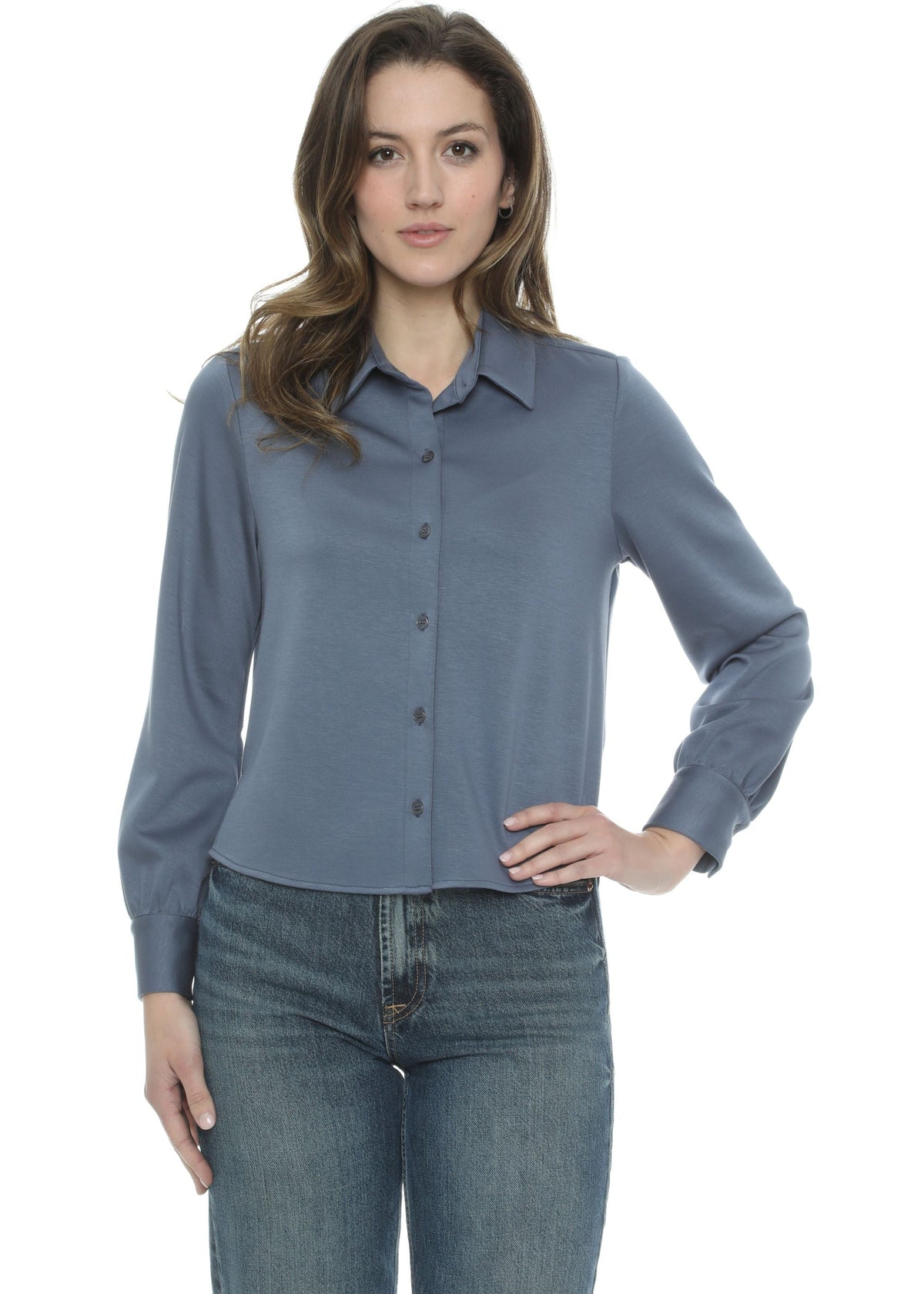 A woman modeling a slate blue long-sleeve button-up blouse with dark buttons, paired with blue jeans, against a plain white background.