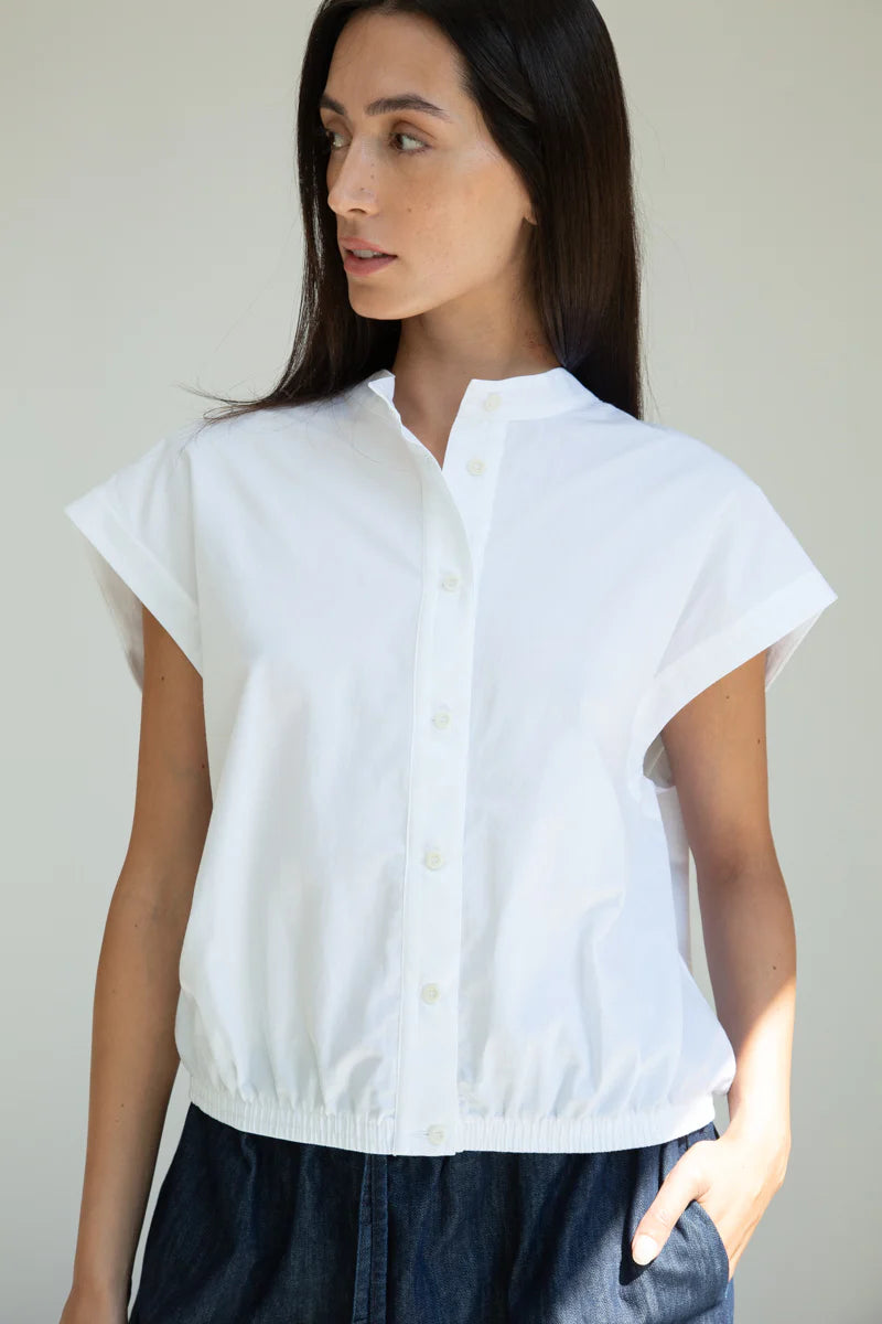Woman wearing a white blouse with short sleeves against a plain background