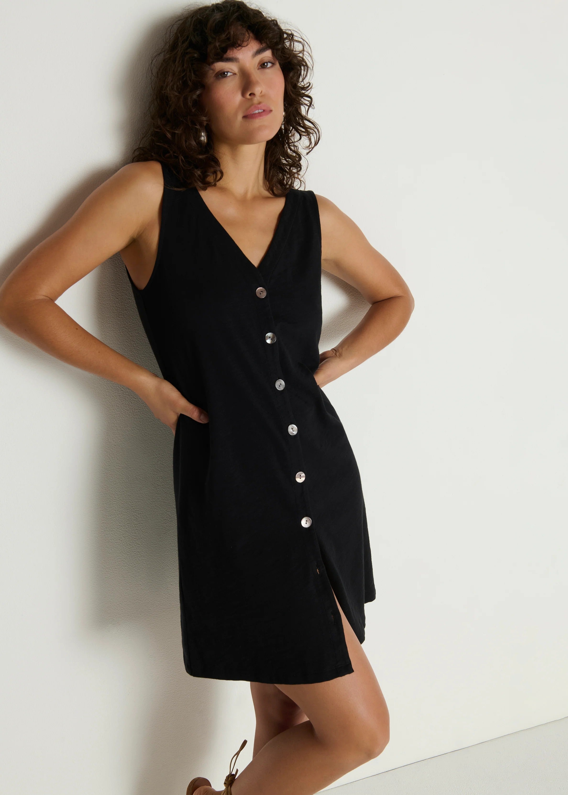 Woman wearing a black sleeveless dress with buttons against a white background
