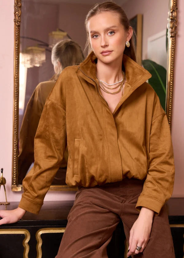 Woman wearing a brown jacket and pants sitting in front of a mirror.