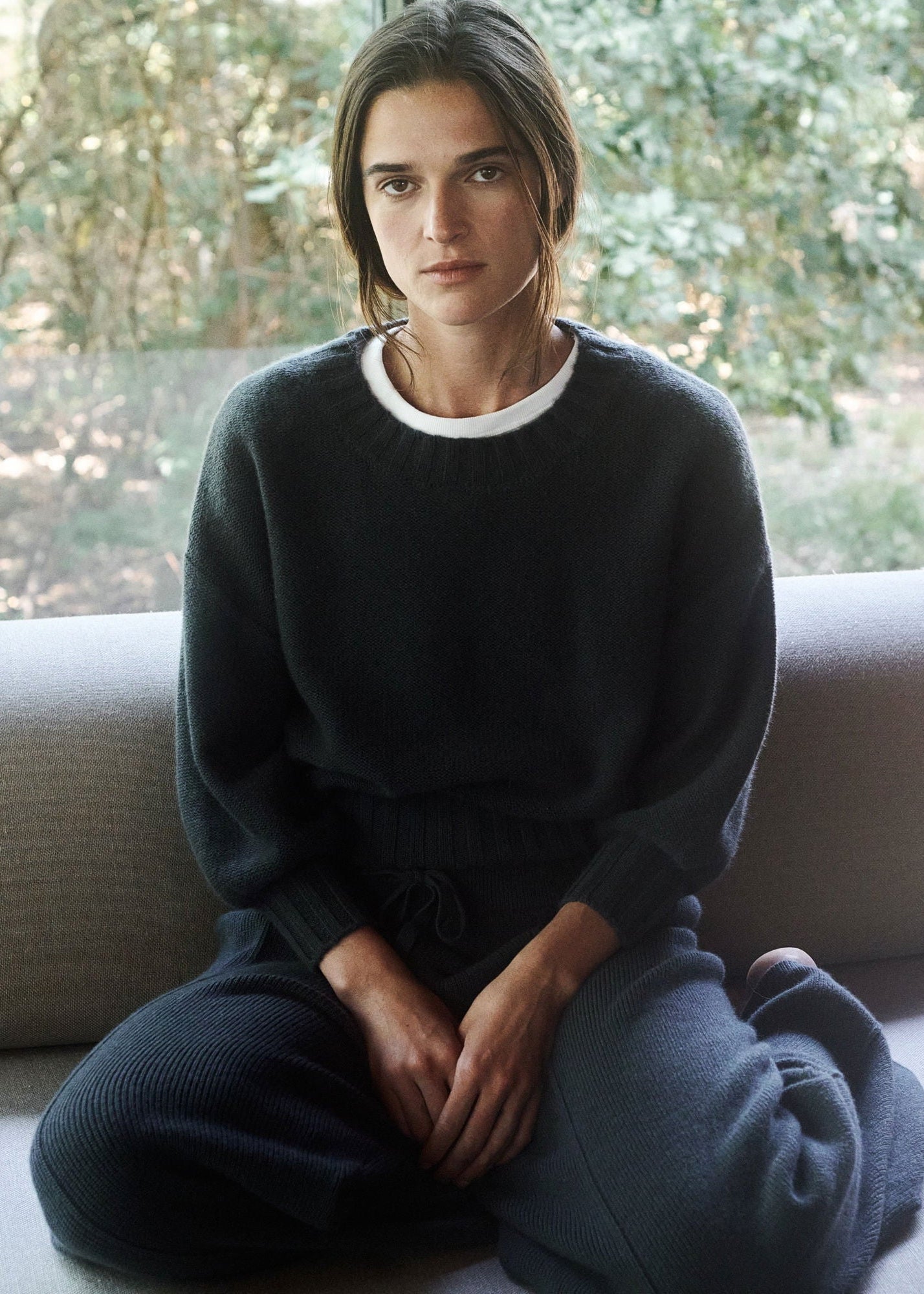Person wearing a dark sweater sitting on a couch with a blurred natural background