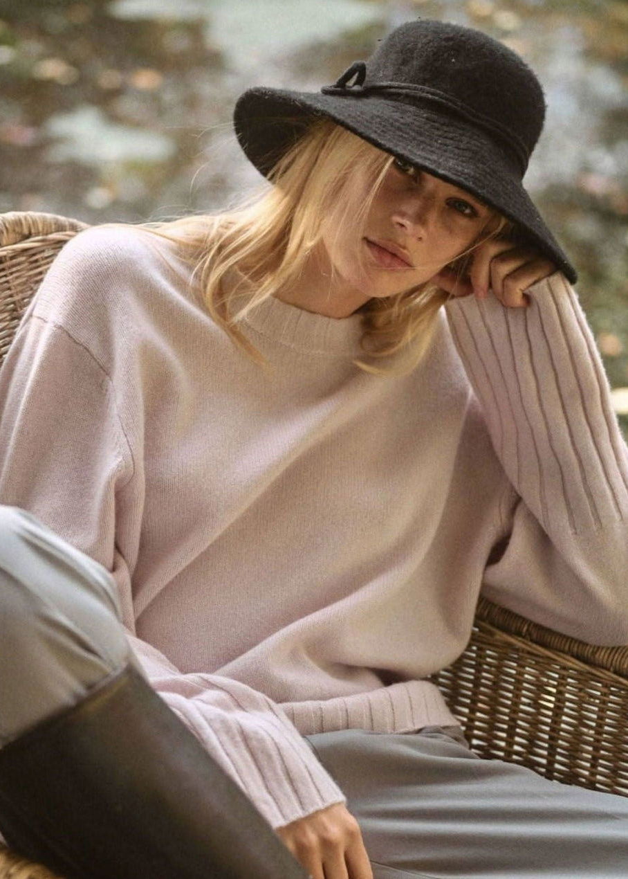 Woman wearing a pink sweater and dark hat sitting outdoors.