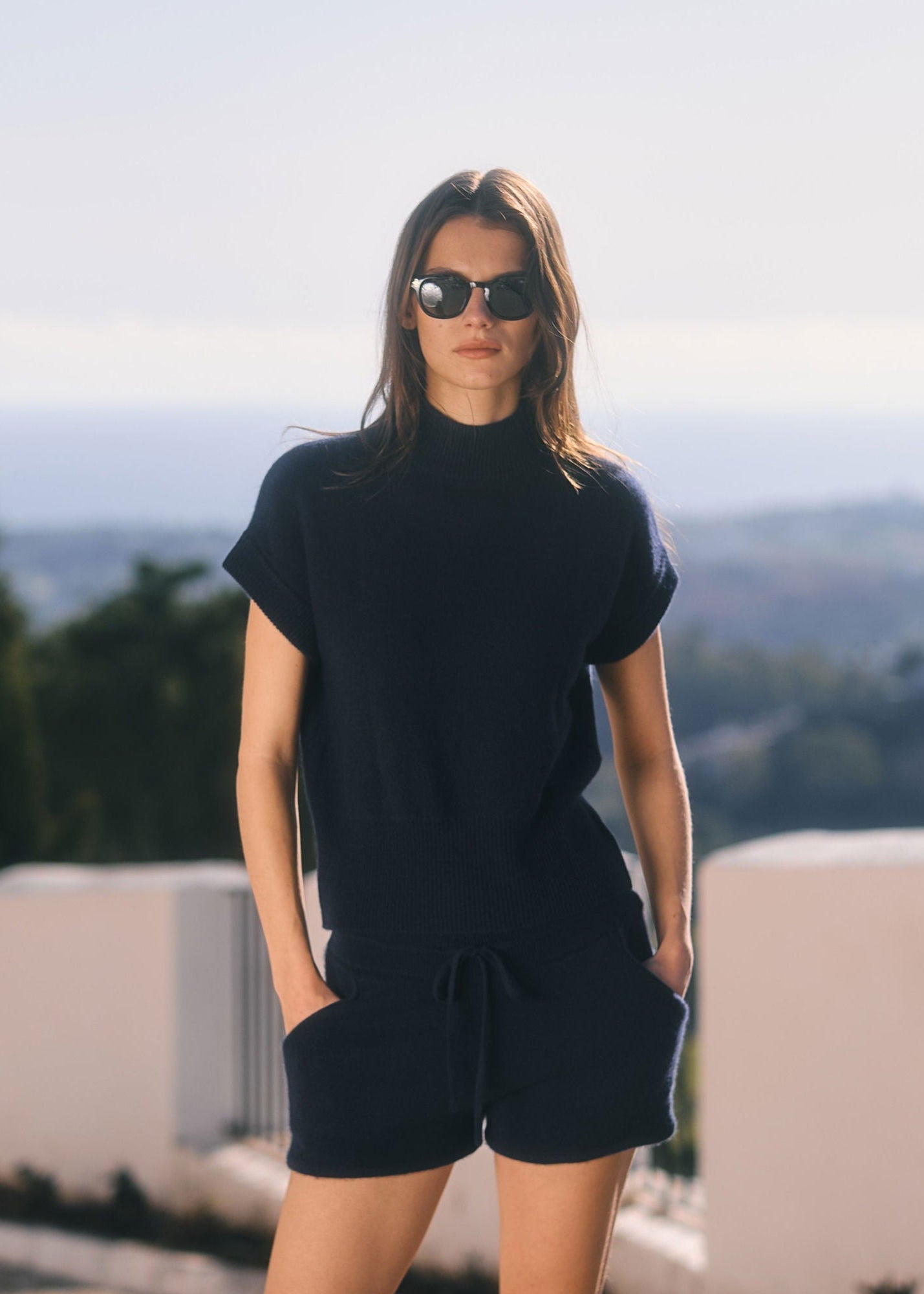 Woman wearing a black outfit with sunglasses against a scenic background