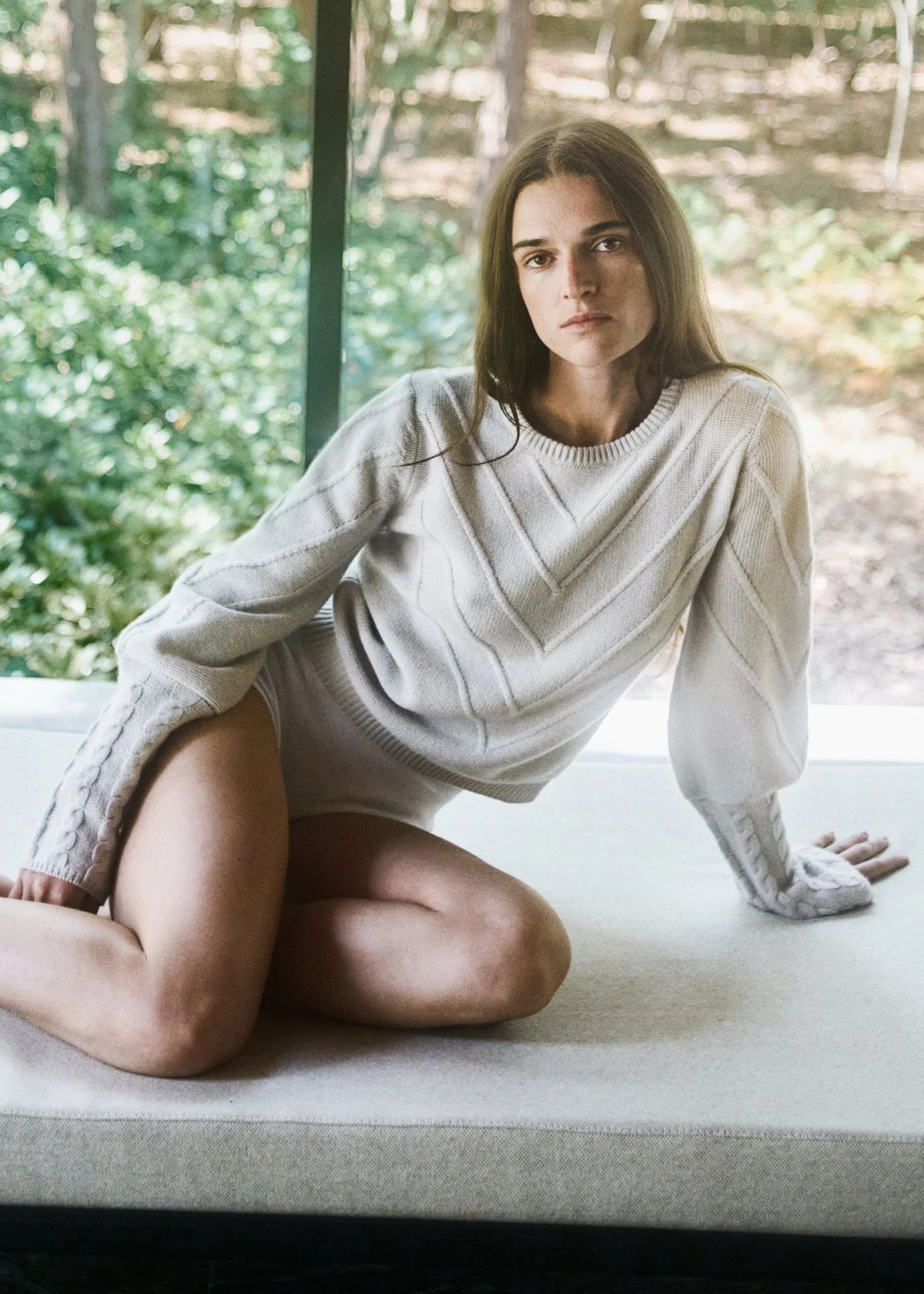 Woman in a white sweater sitting on a windowsill with a natural outdoor background