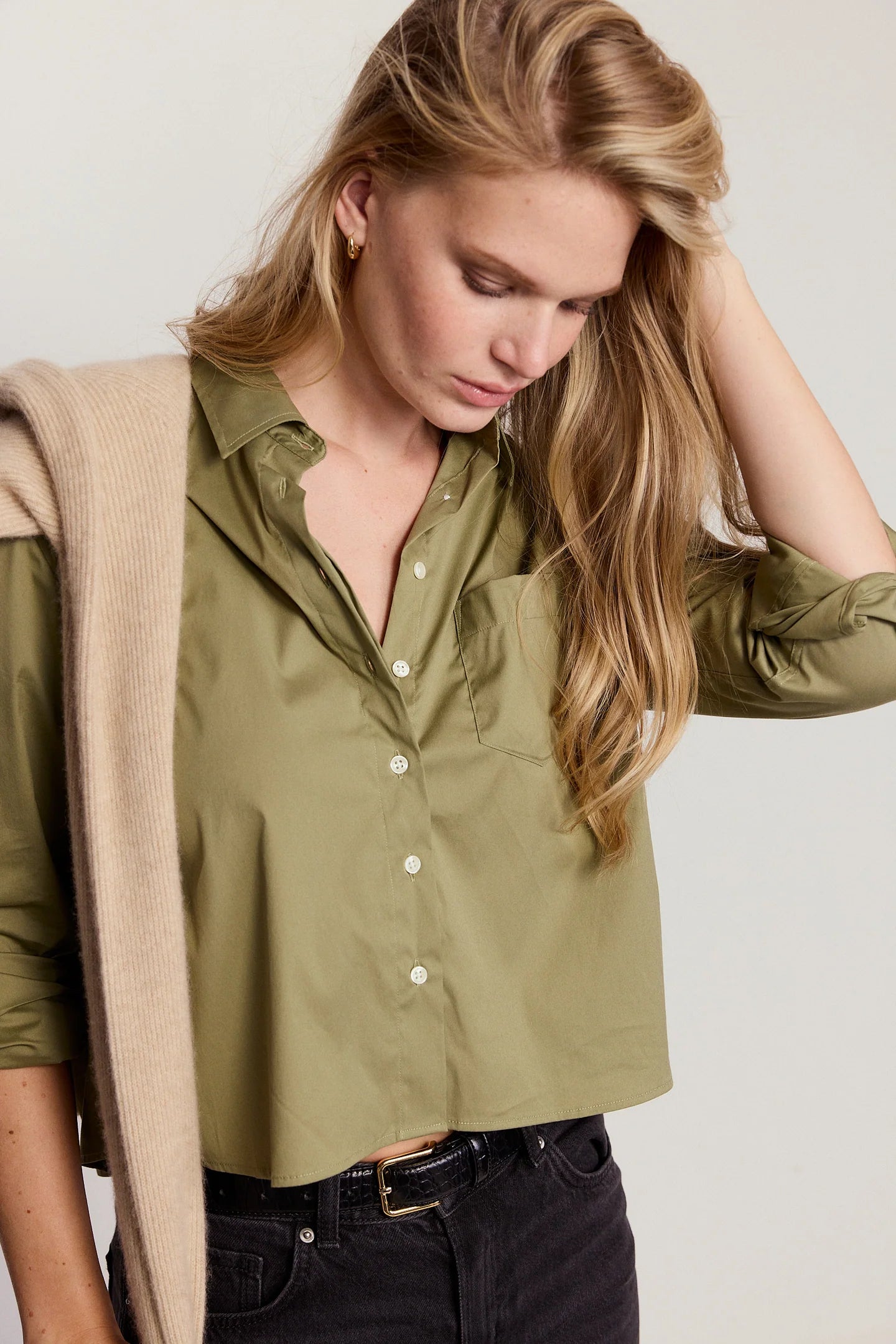 Woman wearing a green shirt with a beige cardigan on a plain background