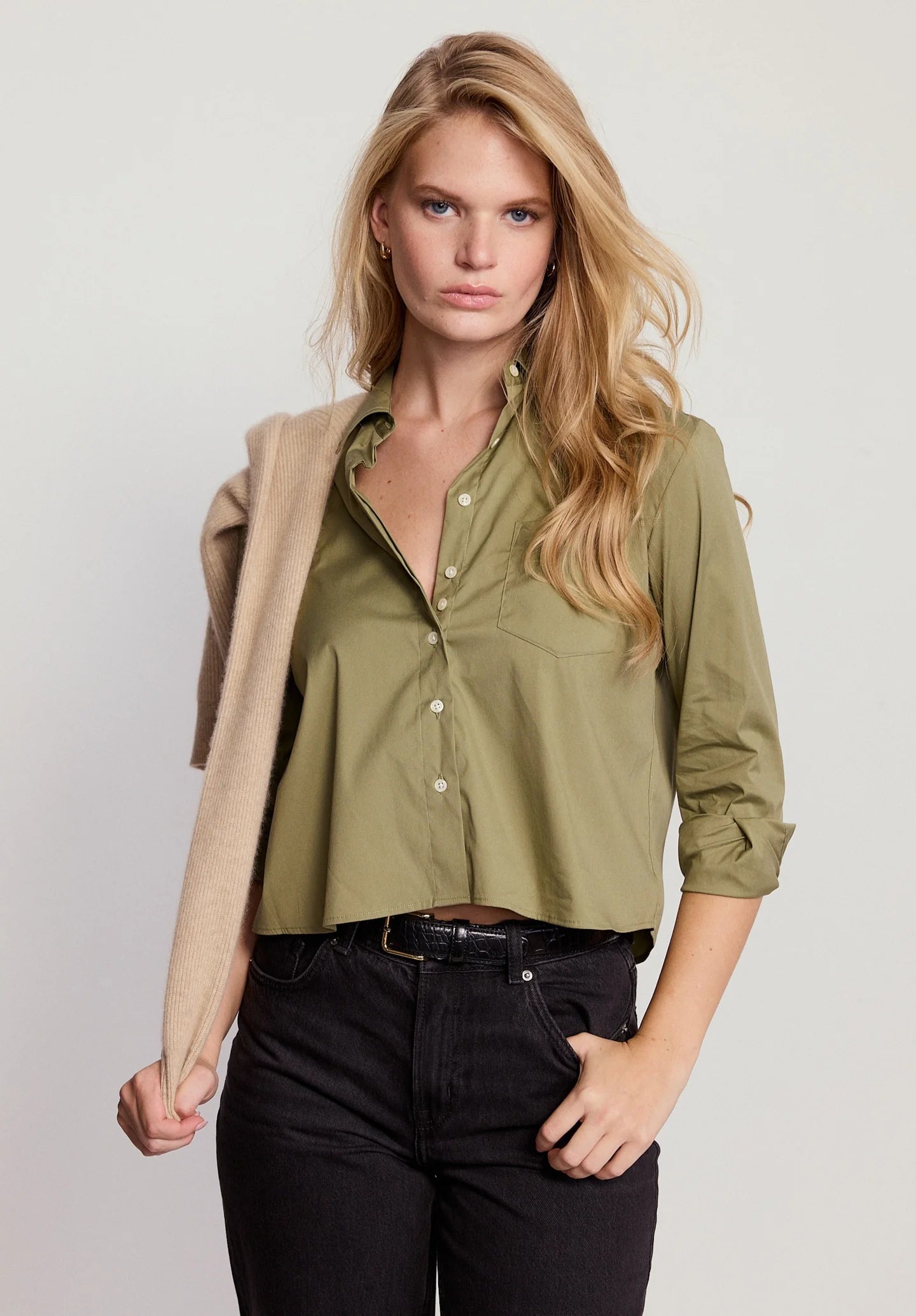 Woman wearing a green shirt with rolled-up sleeves and a beige cardigan on a plain background