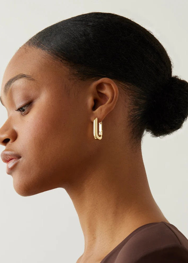 Woman wearing gold hoop earrings with a neutral background