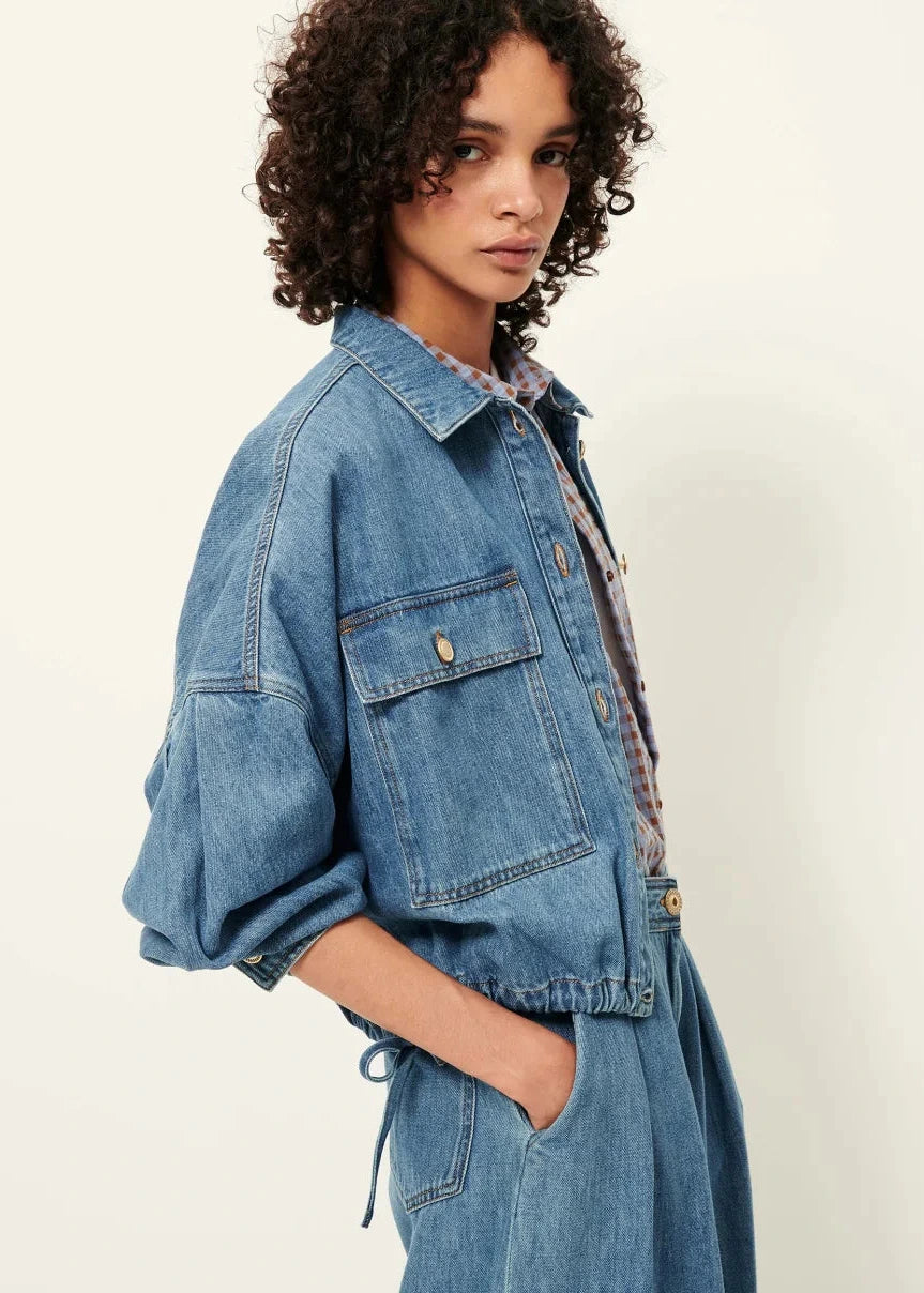 Woman wearing a blue denim jacket and dress against a white background