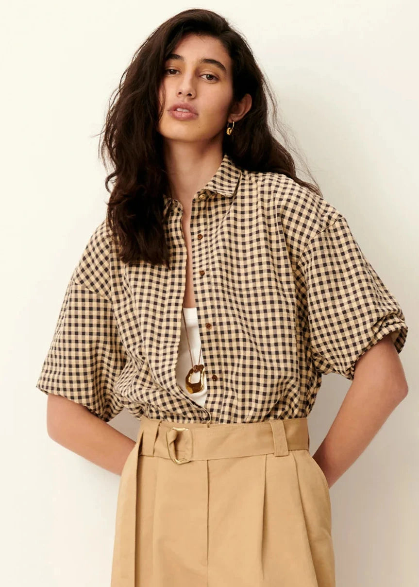 Woman wearing a checkered shirt and beige pants against a plain background