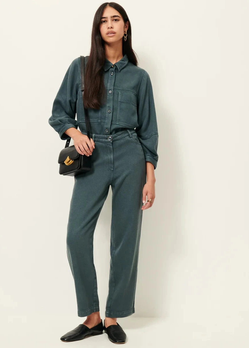 Woman wearing a teal outfit with a black handbag on a white background
