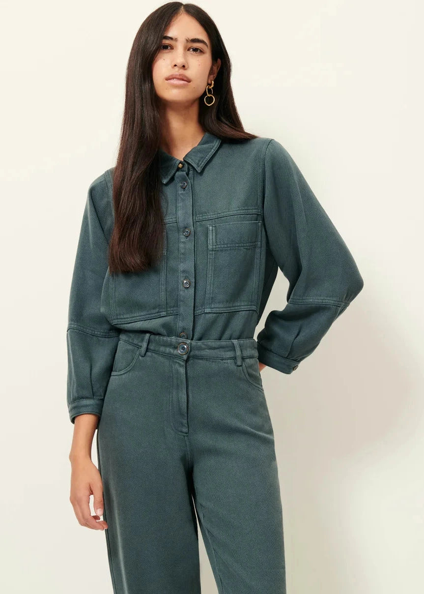 Woman wearing a green denim jumpsuit against a white background