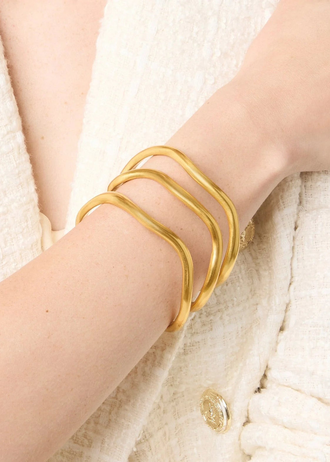 Gold bracelet on a person's wrist against a textured white background