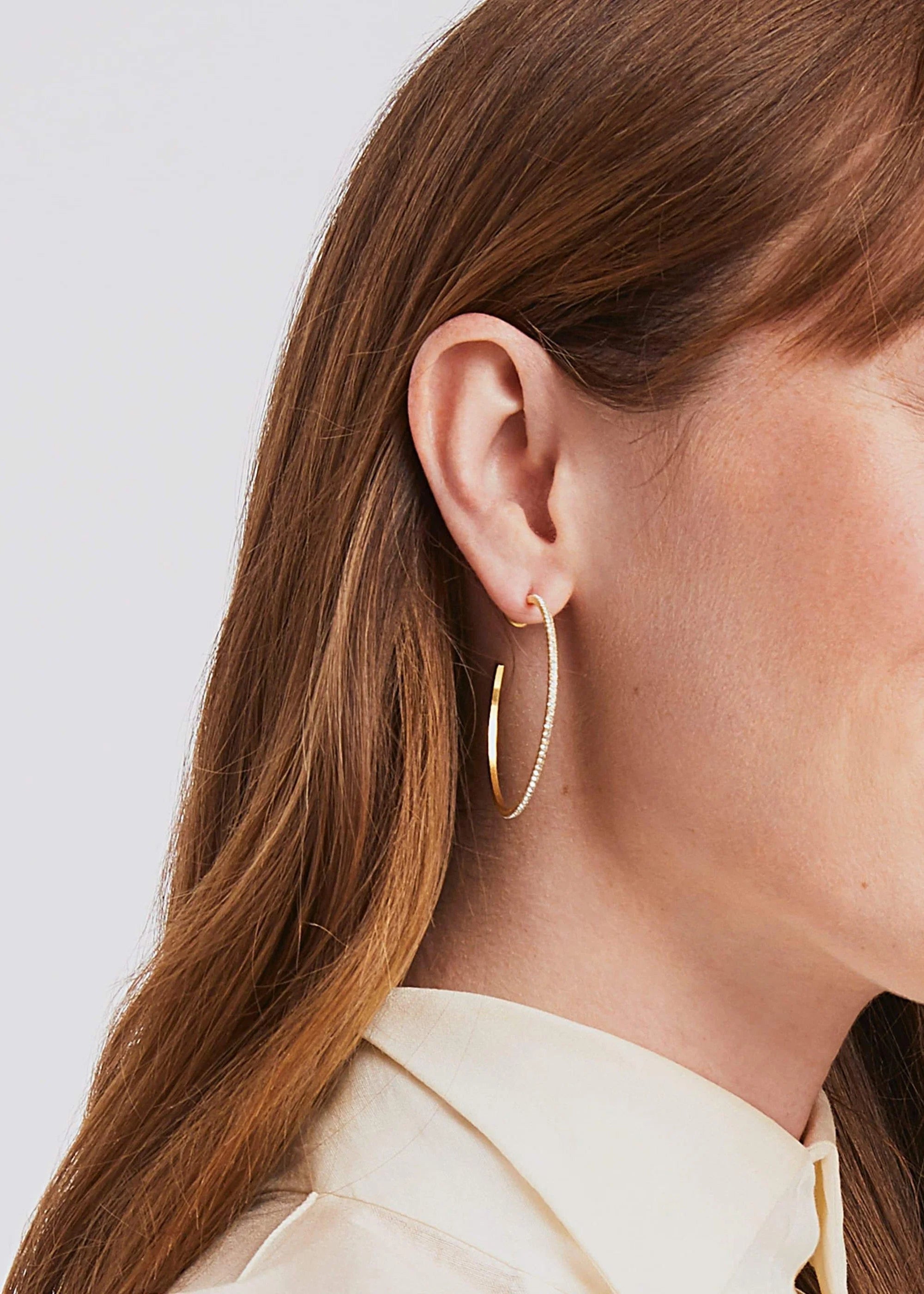 Close-up of a woman wearing gold hoop earrings with a plain background
